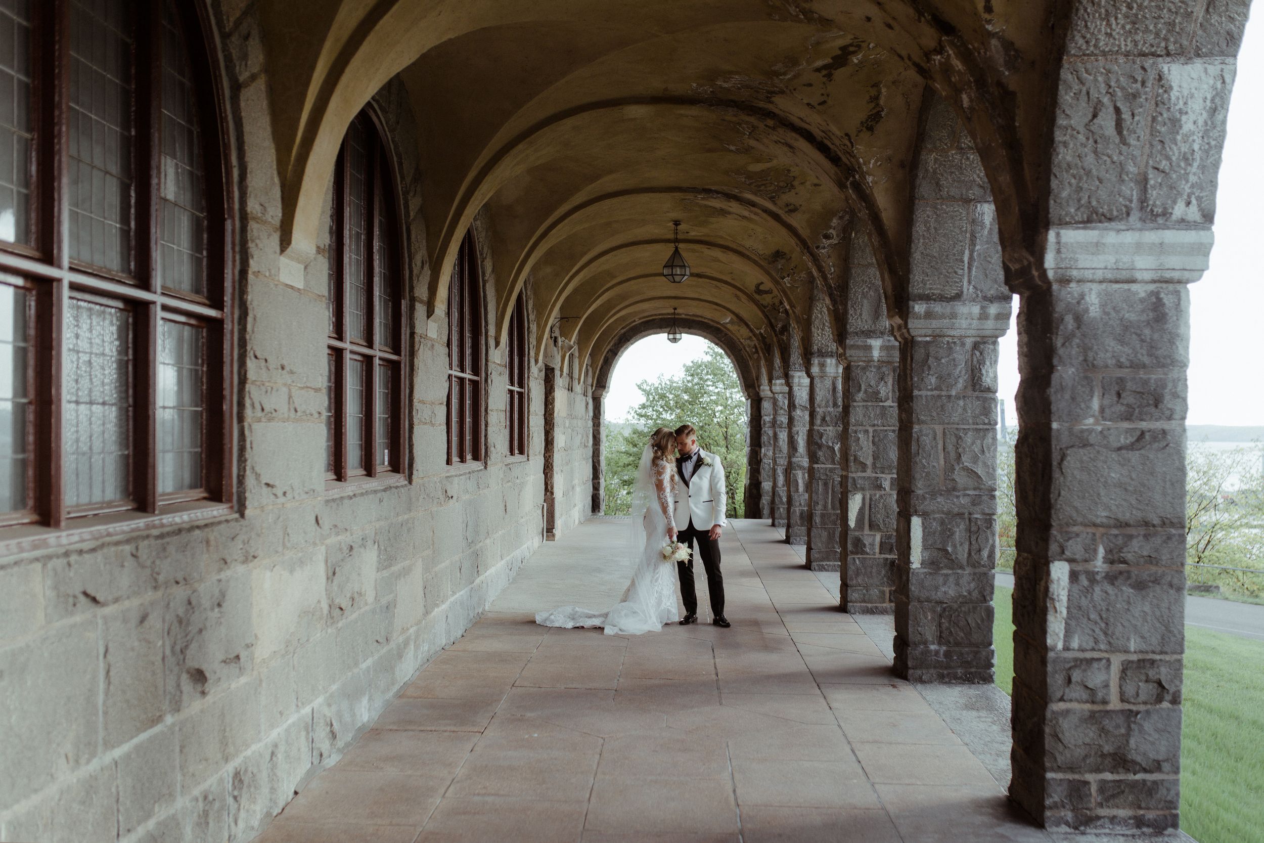 Stone arched corridor with sunlit columns in a historic building creating dramatic shadows and perspective.