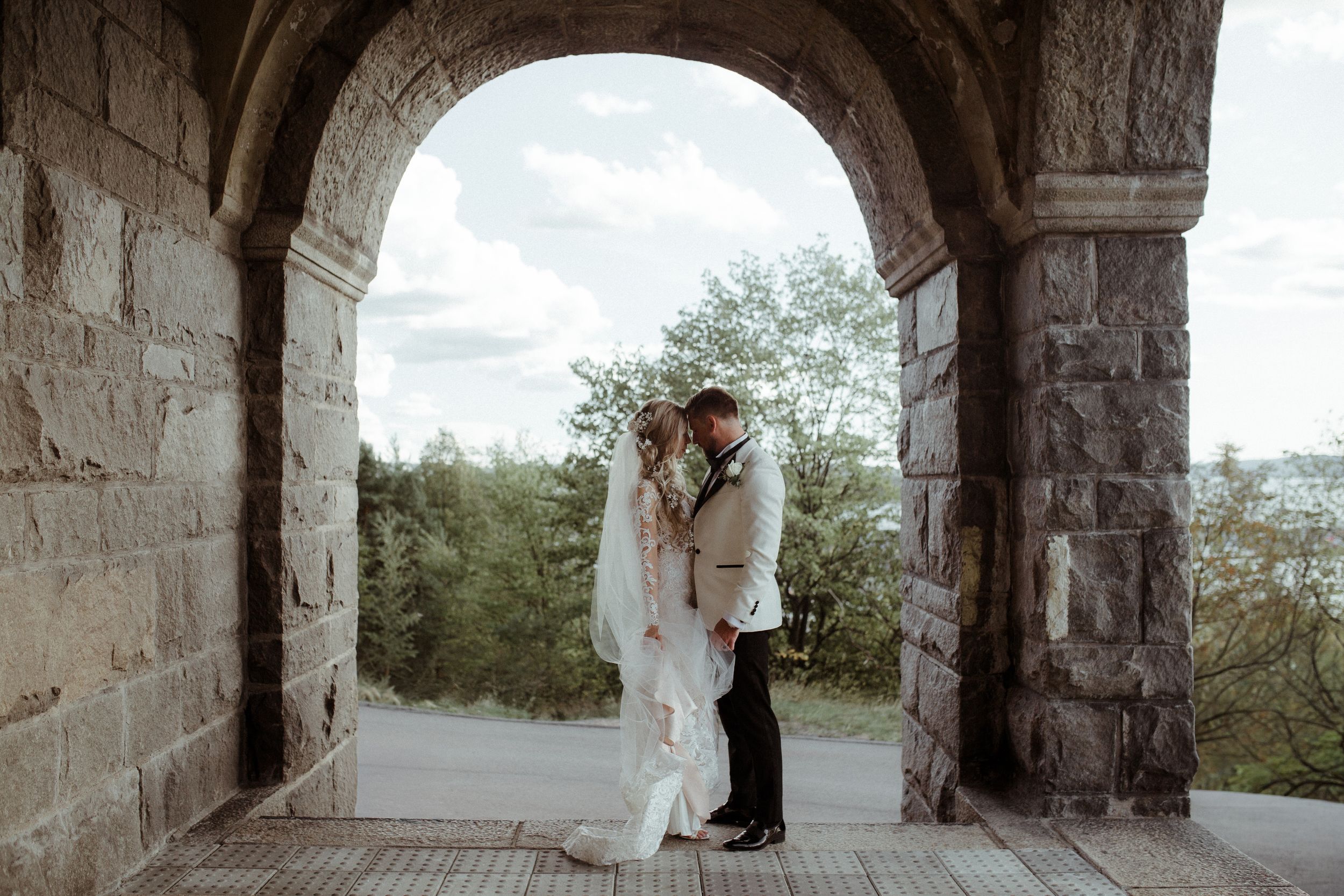 Romantic wedding moment captured under stone archway with natural landscape backdrop.