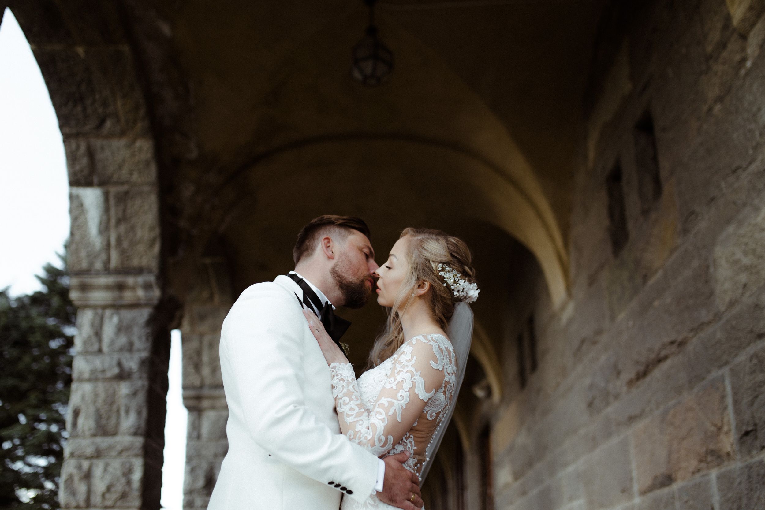Stone archway frames romantic wedding moment in historic architectural setting.