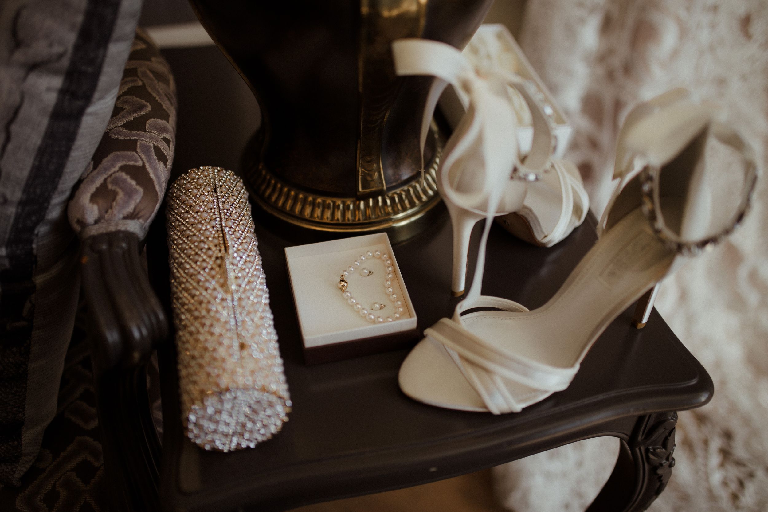Wedding accessories including lace details and elegant white shoes arranged on dark surface.
