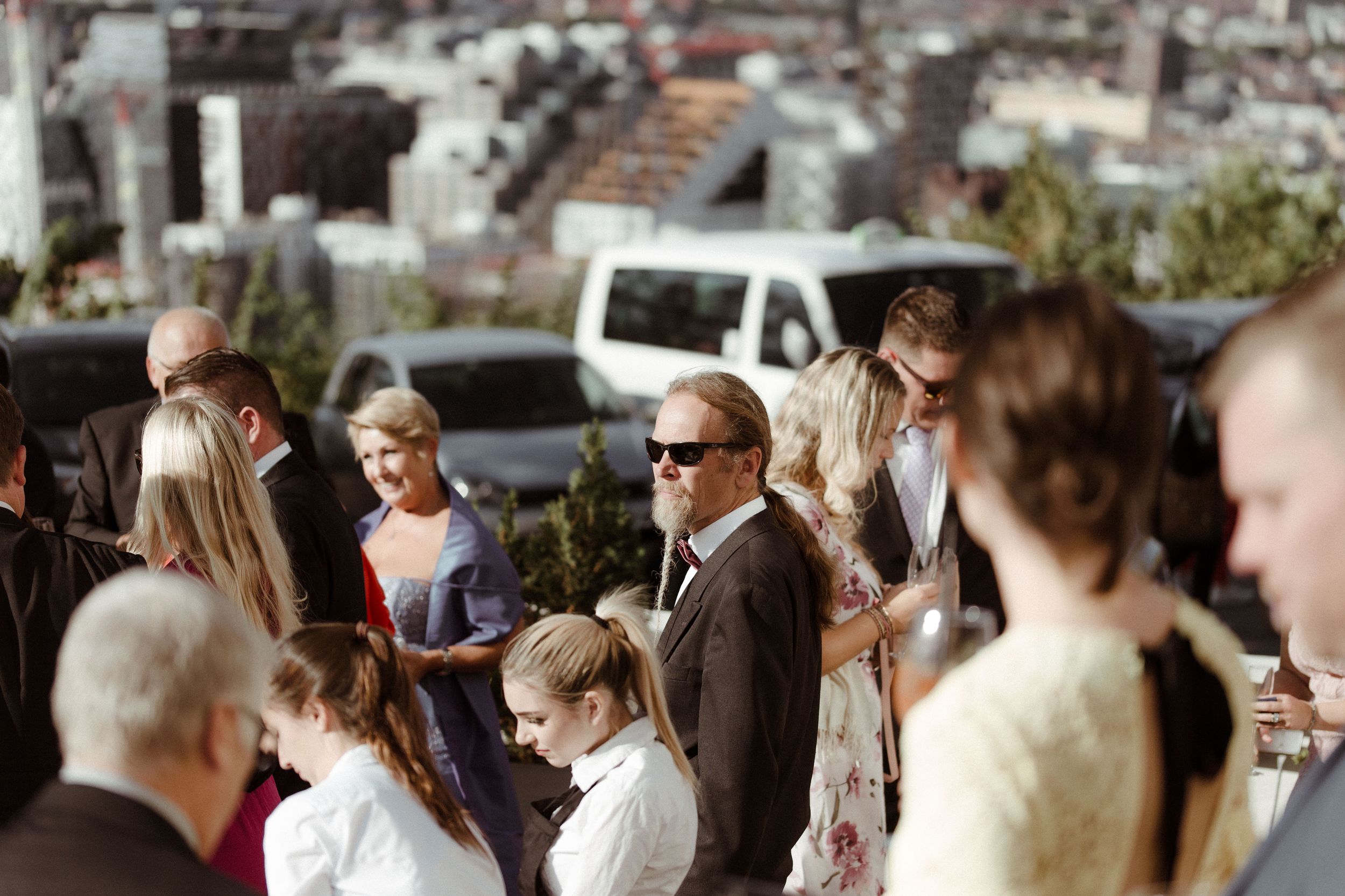 Wedding guests gather outdoors for a celebratory moment on a sunny day.