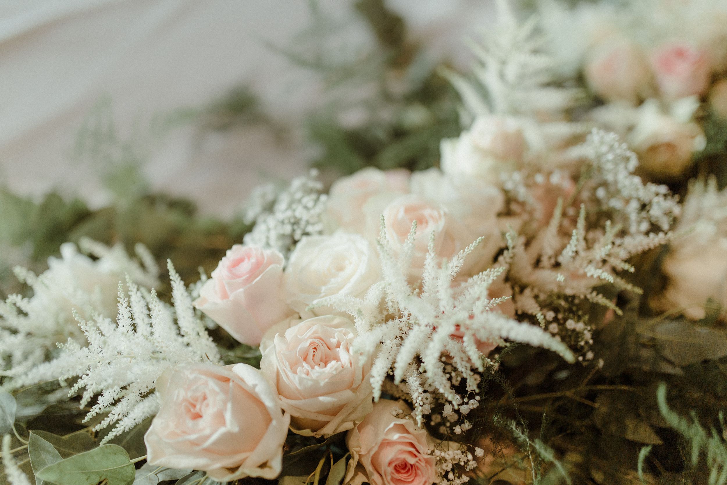 Close-up detail of pale pink roses and delicate white flowers in an elegant wedding floral arrangement.