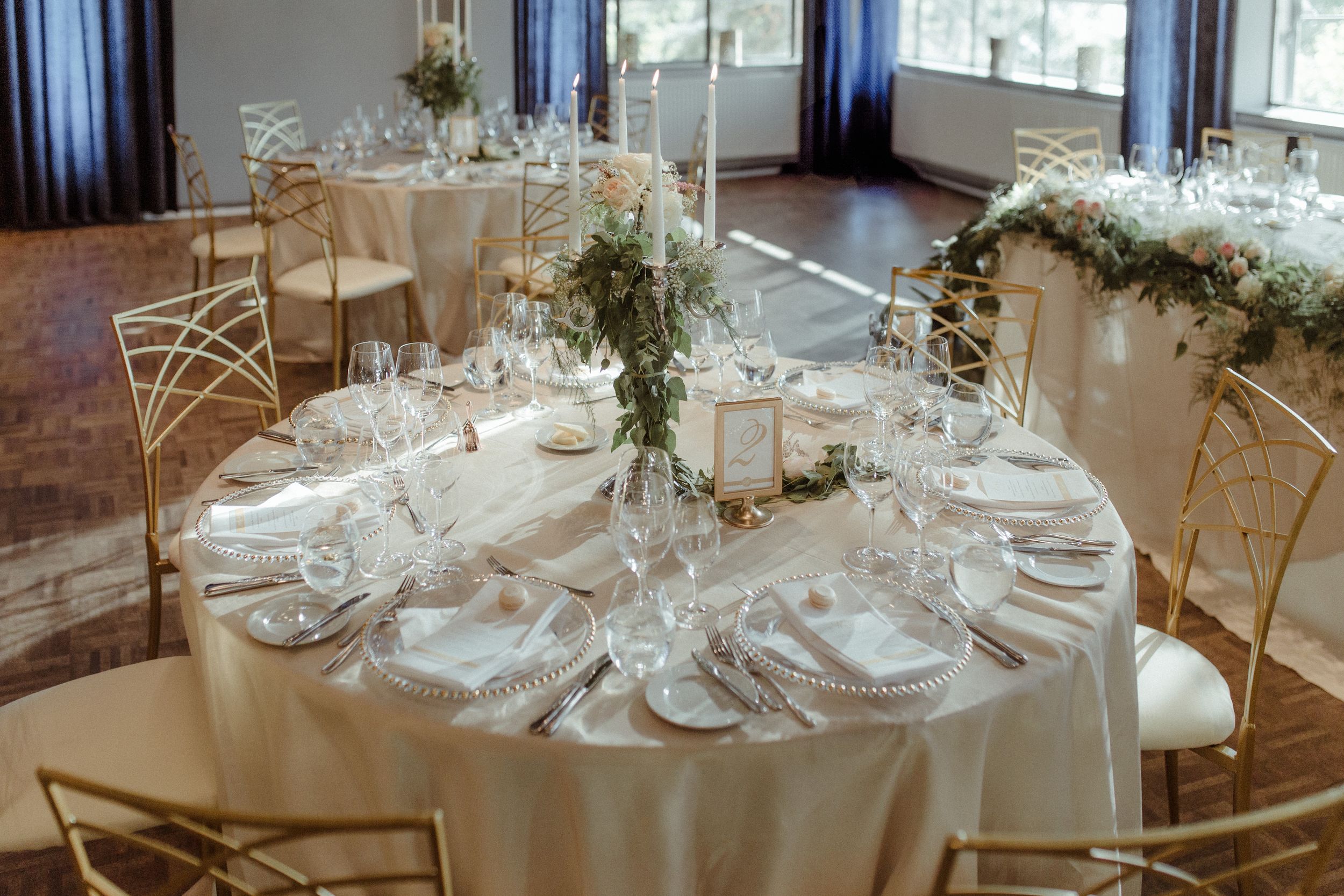 Elegant wedding reception tables set with white linens, centerpieces and formal place settings in natural light.