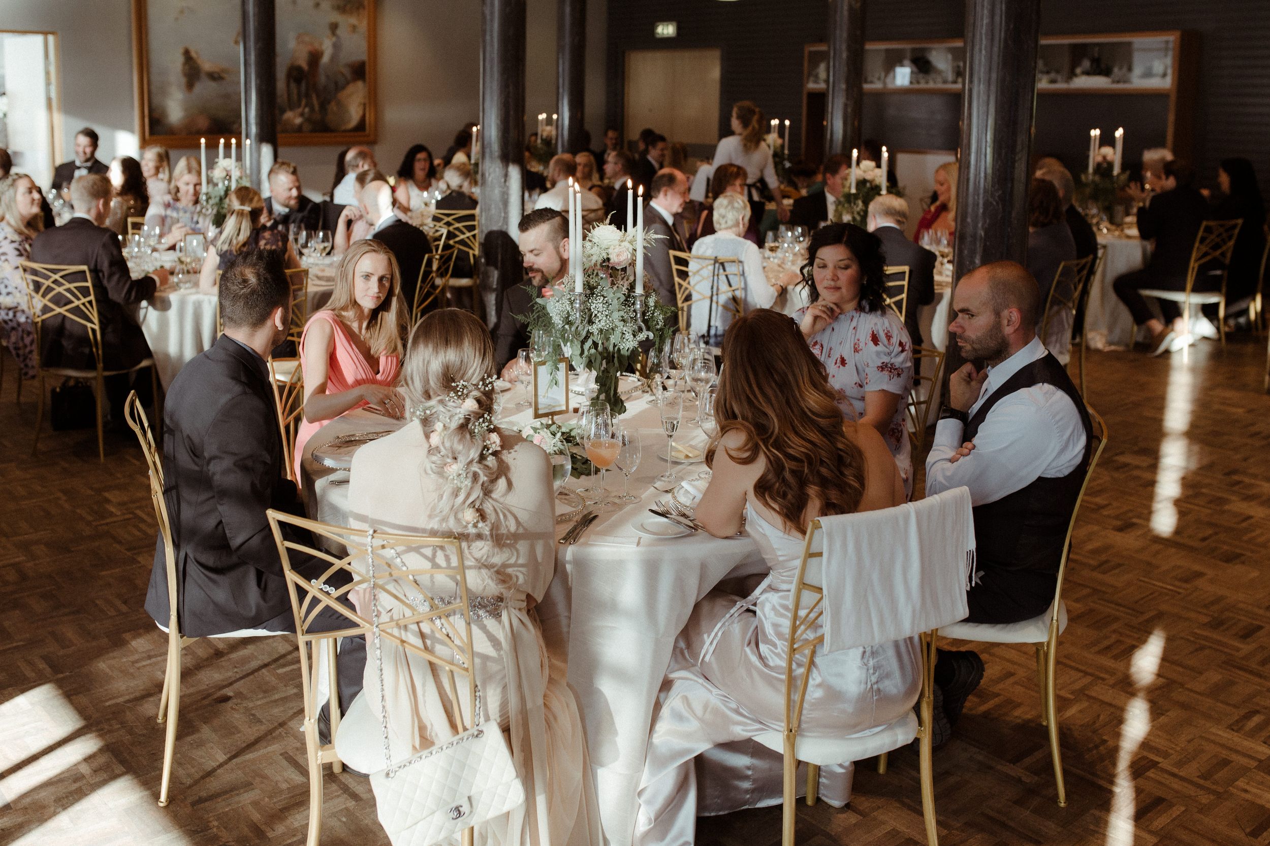 Wedding celebration in a rustic indoor venue with guests mingling around decorated tables.