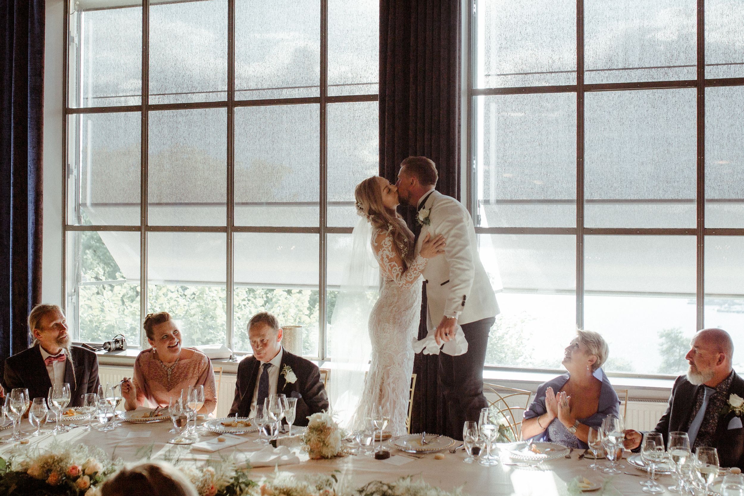 Natural light streams through large windows at an elegant dining event with white tablecloths.