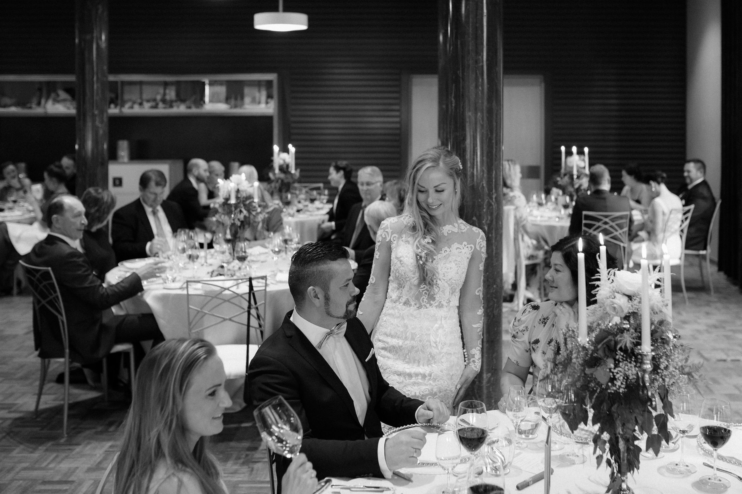Elegant wedding reception tables set with white linens and floral centerpieces in a dimly lit venue.
