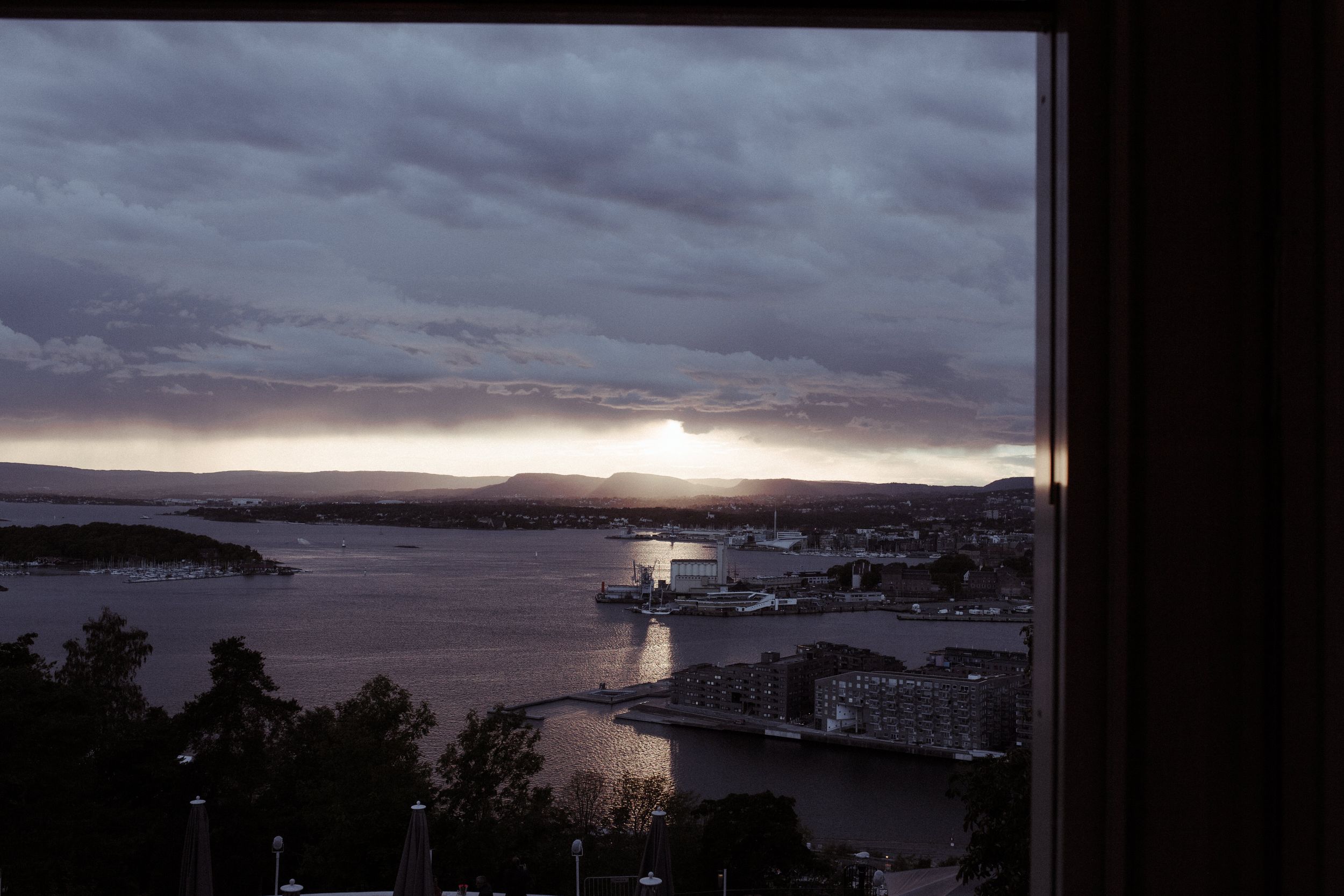 Dramatic sunset sky over coastal city skyline viewed through large windows.