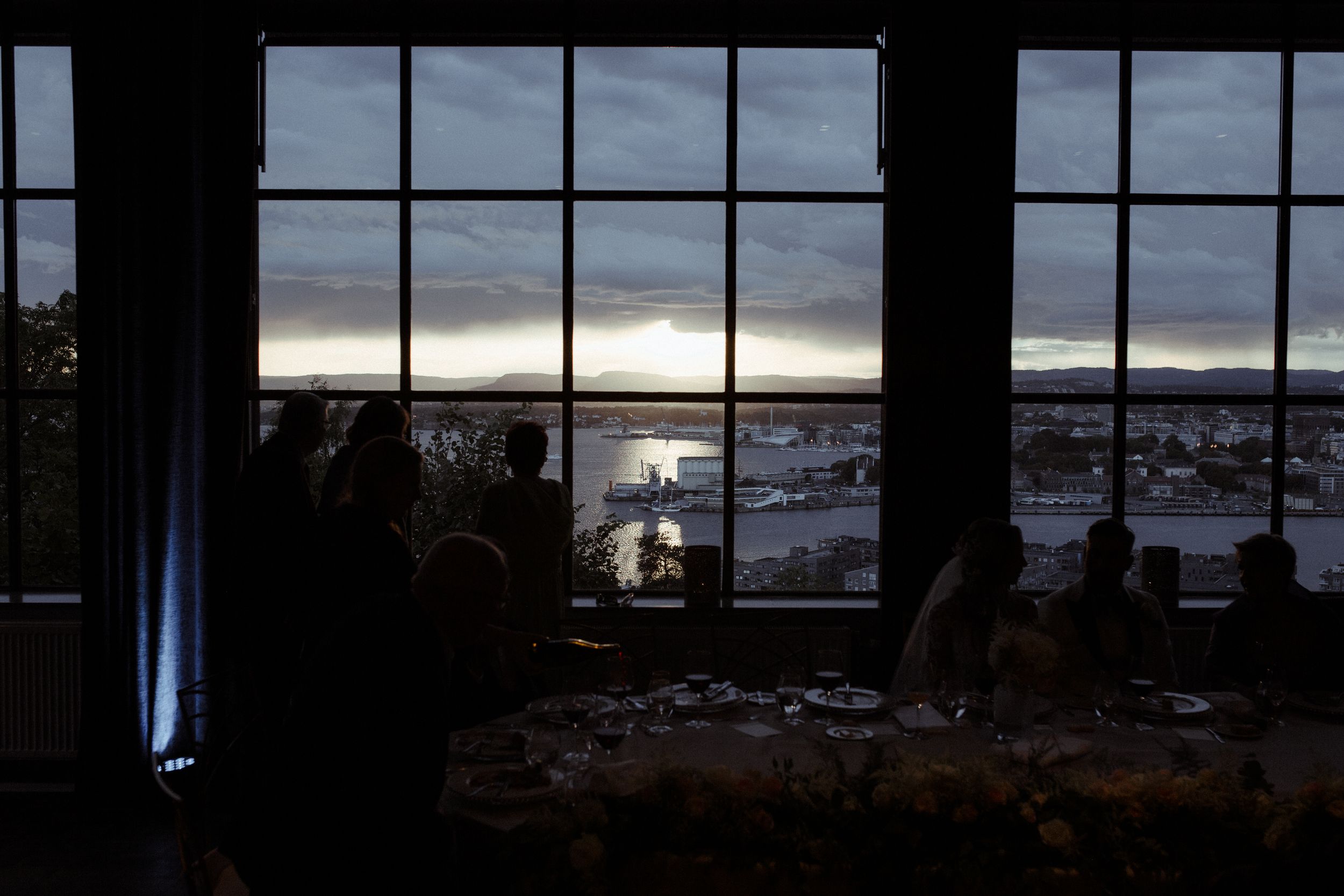 Scenic view of a harbor at sunset through large windows in a dimly lit room.