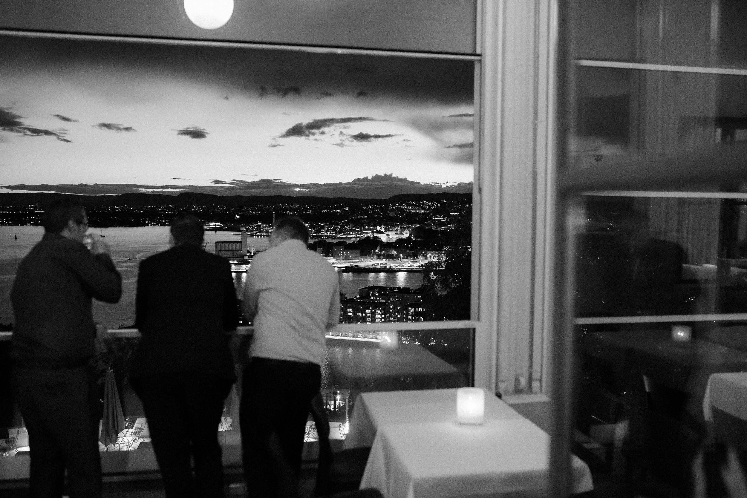 Black and white panoramic view of a cityscape through large windows at dusk.