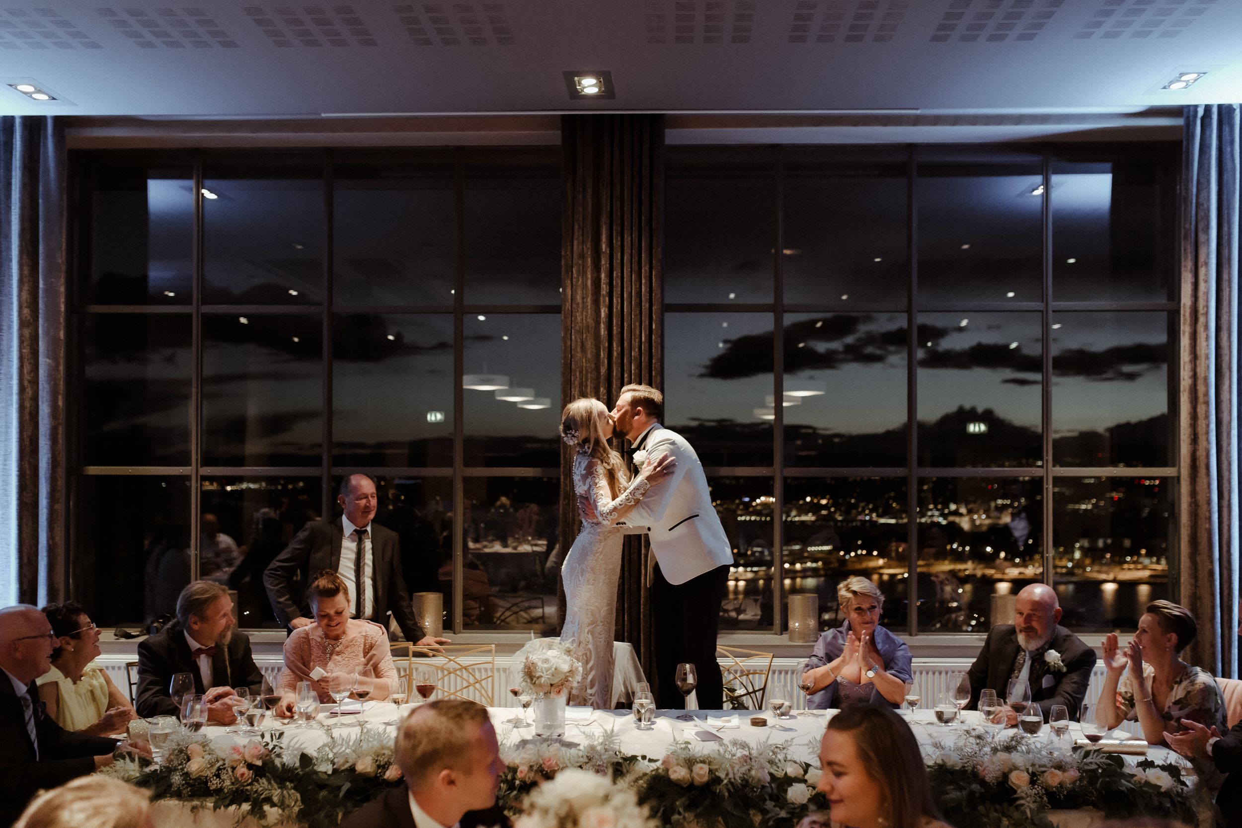 Elegant wedding reception hall with floor-to-ceiling windows overlooking city lights at dusk.