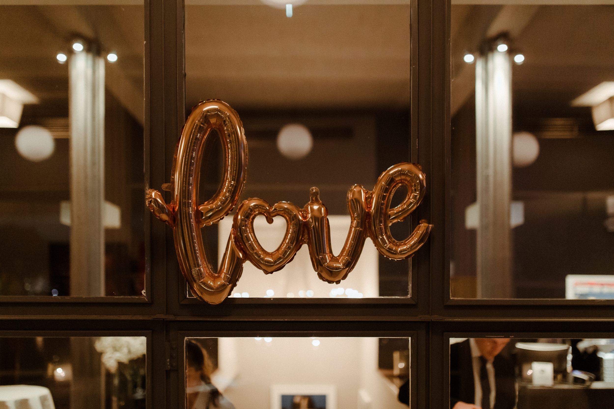 Warm-lit event space with decorative gold balloon letters and hanging globe lights.