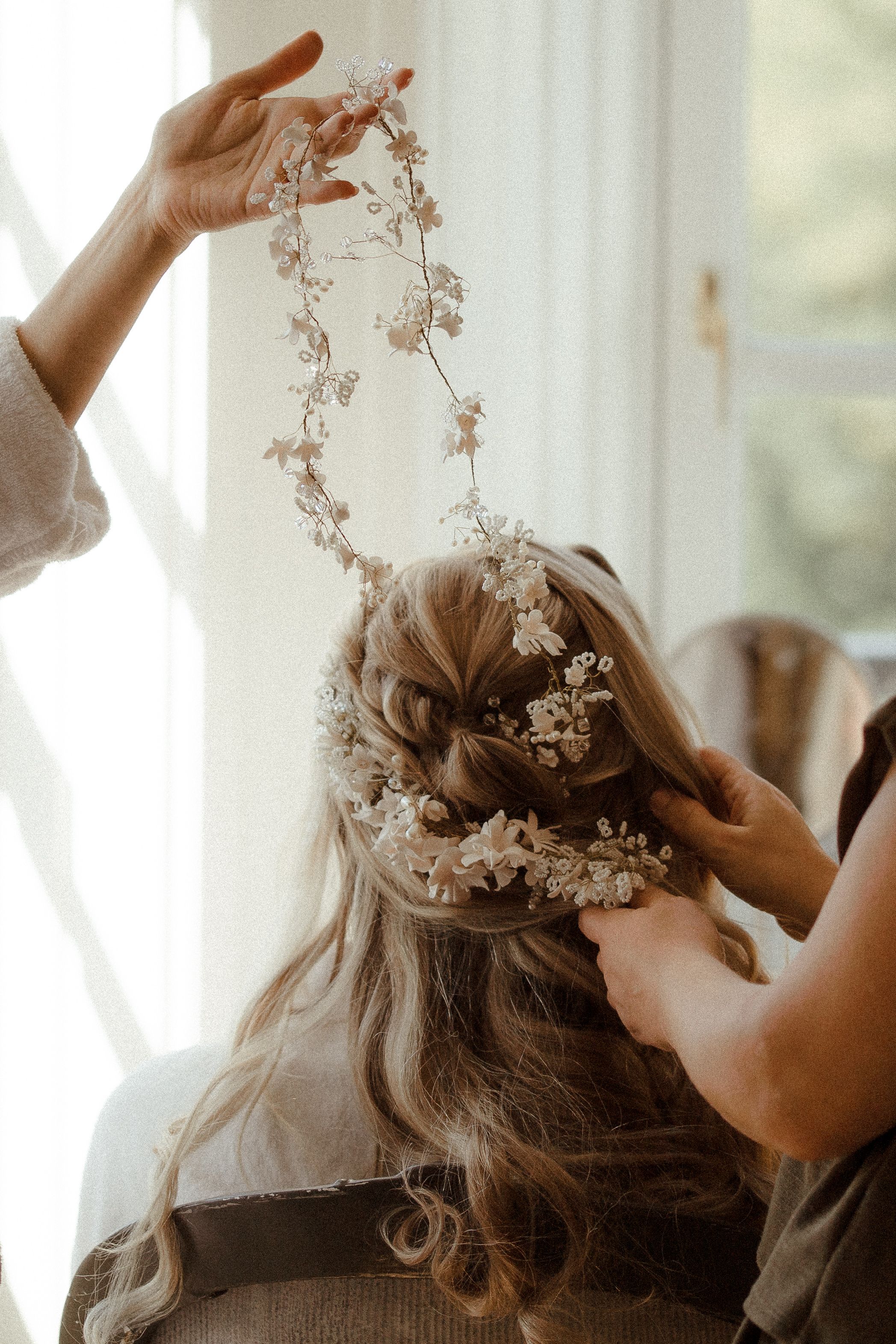 Delicate white floral hairpiece being carefully arranged in an elegant updo hairstyle.