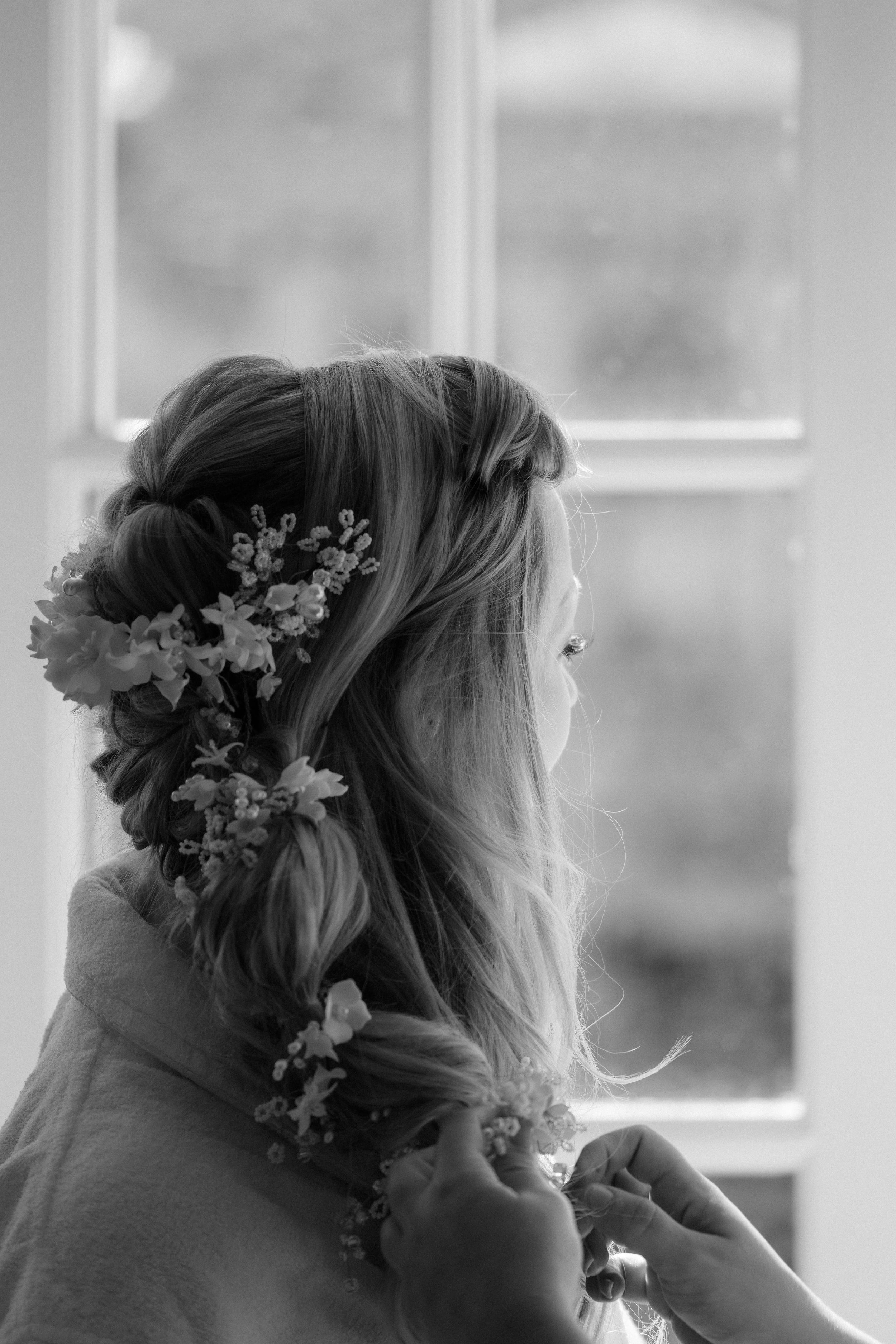Black and white photo of a bride with floral hair accessories getting ready on her wedding day.