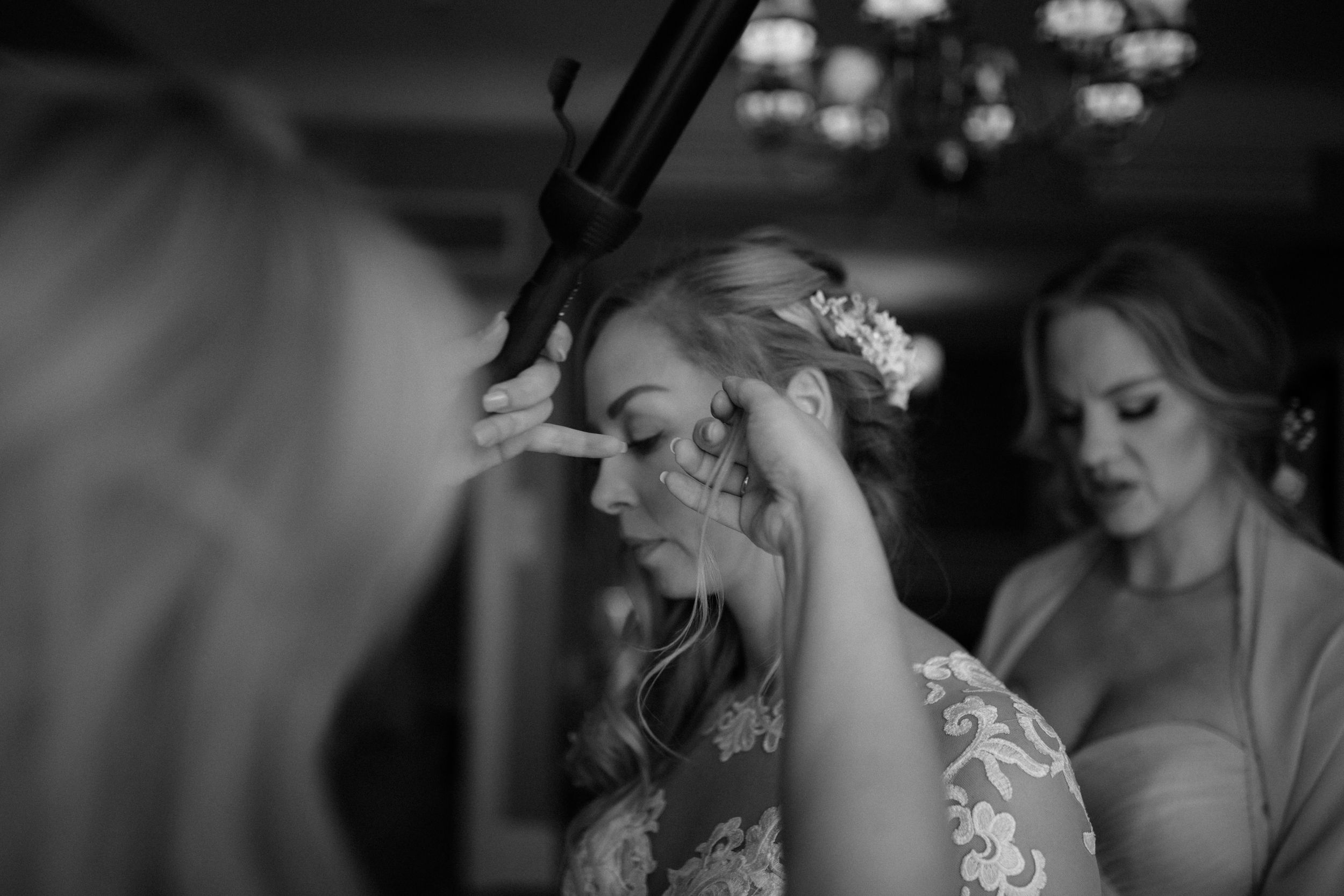 Black and white photograph of wedding day preparations with soft lighting and chandeliers.