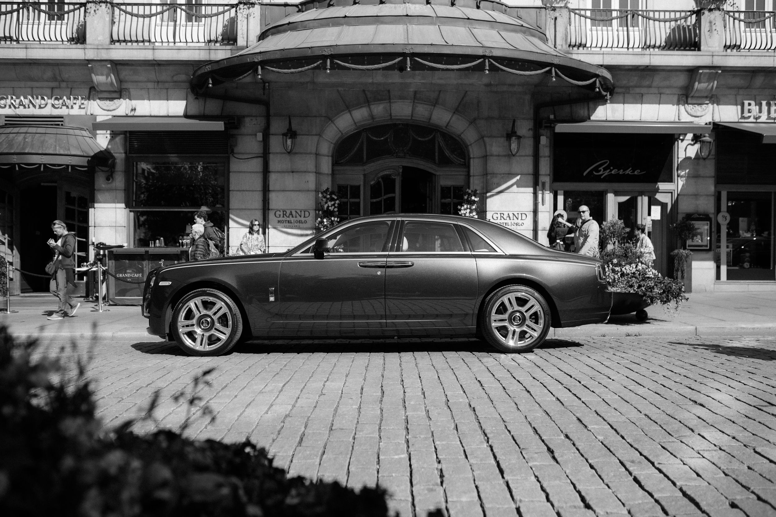 Luxury black Rolls Royce parked on cobblestone street in front of historic building.
