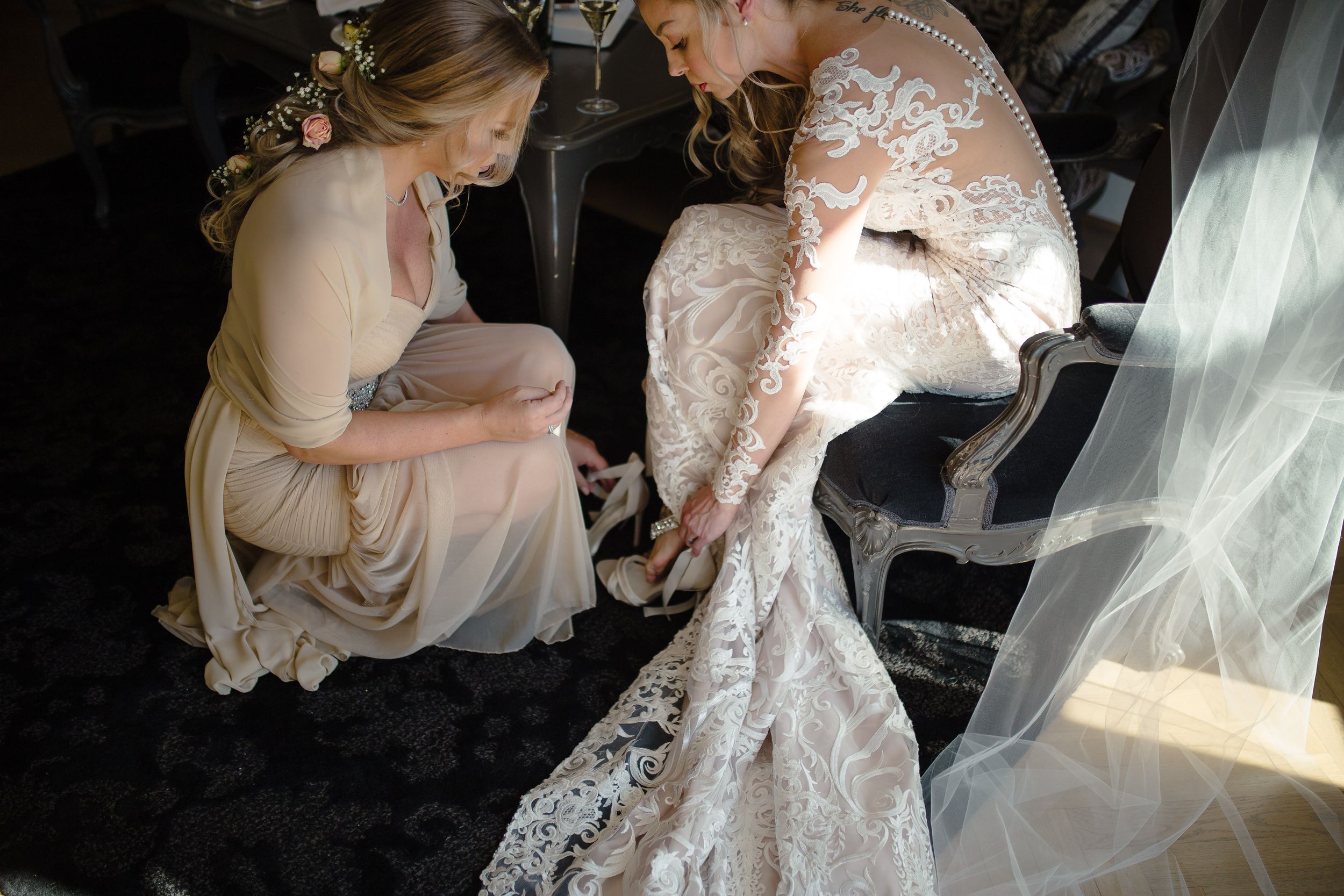 Delicate lace wedding dress being adjusted in soft natural lighting.
