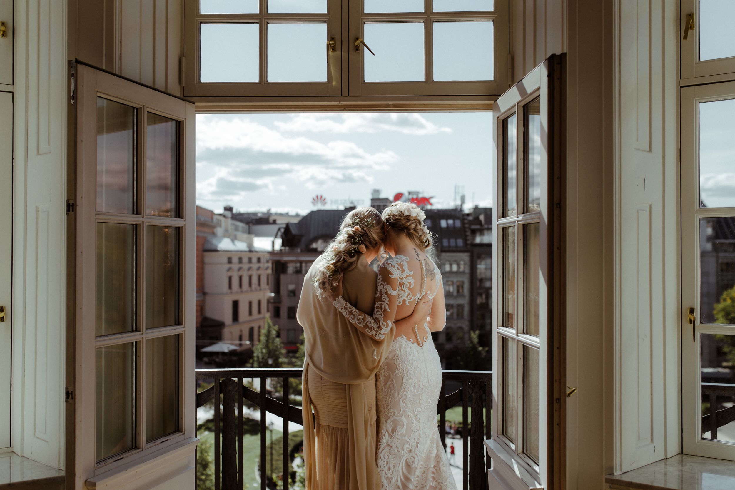 Two people embrace by open French doors overlooking a city skyline on a cloudy day.