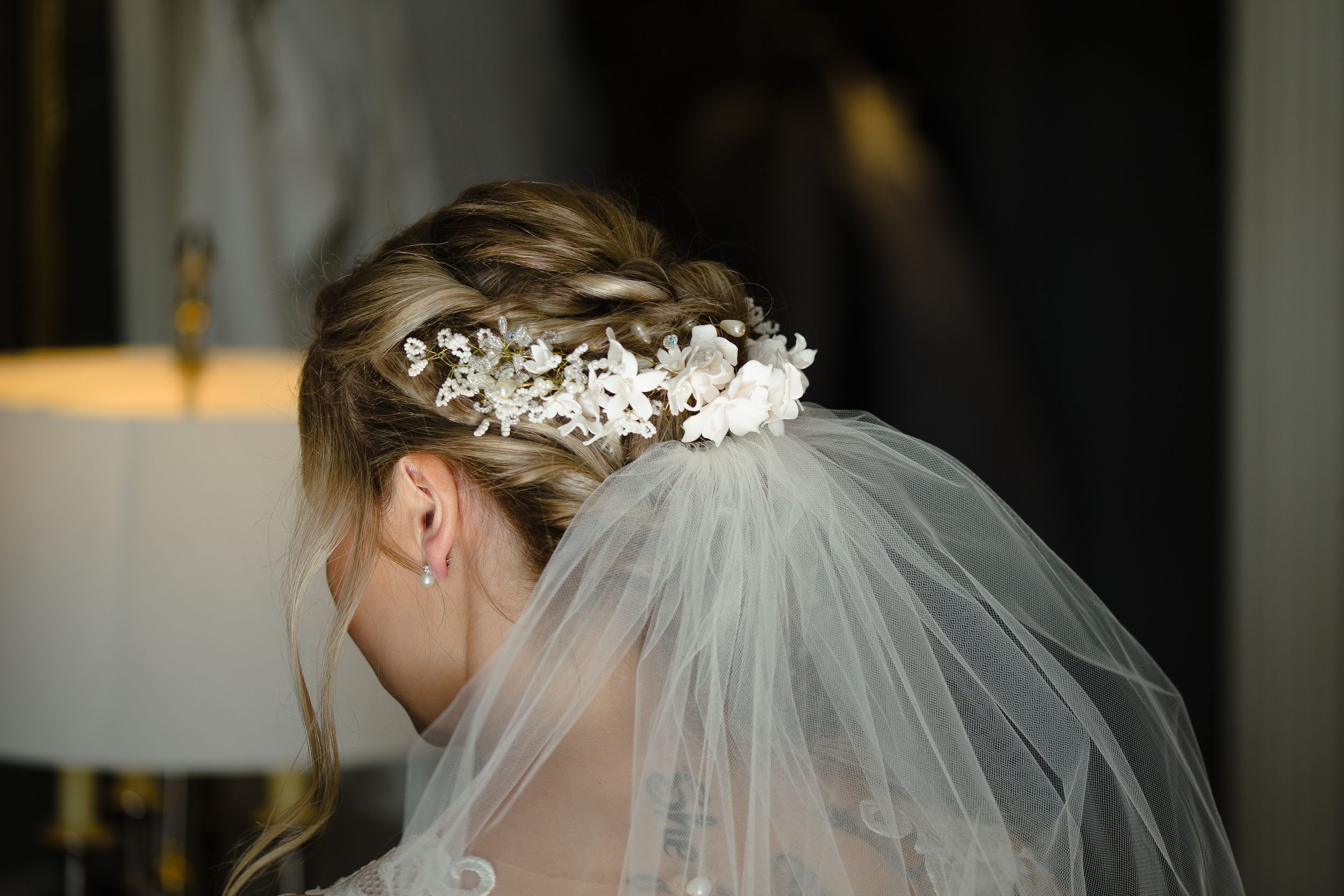 Bride wearing a delicate floral headpiece and veil in dramatic lighting.