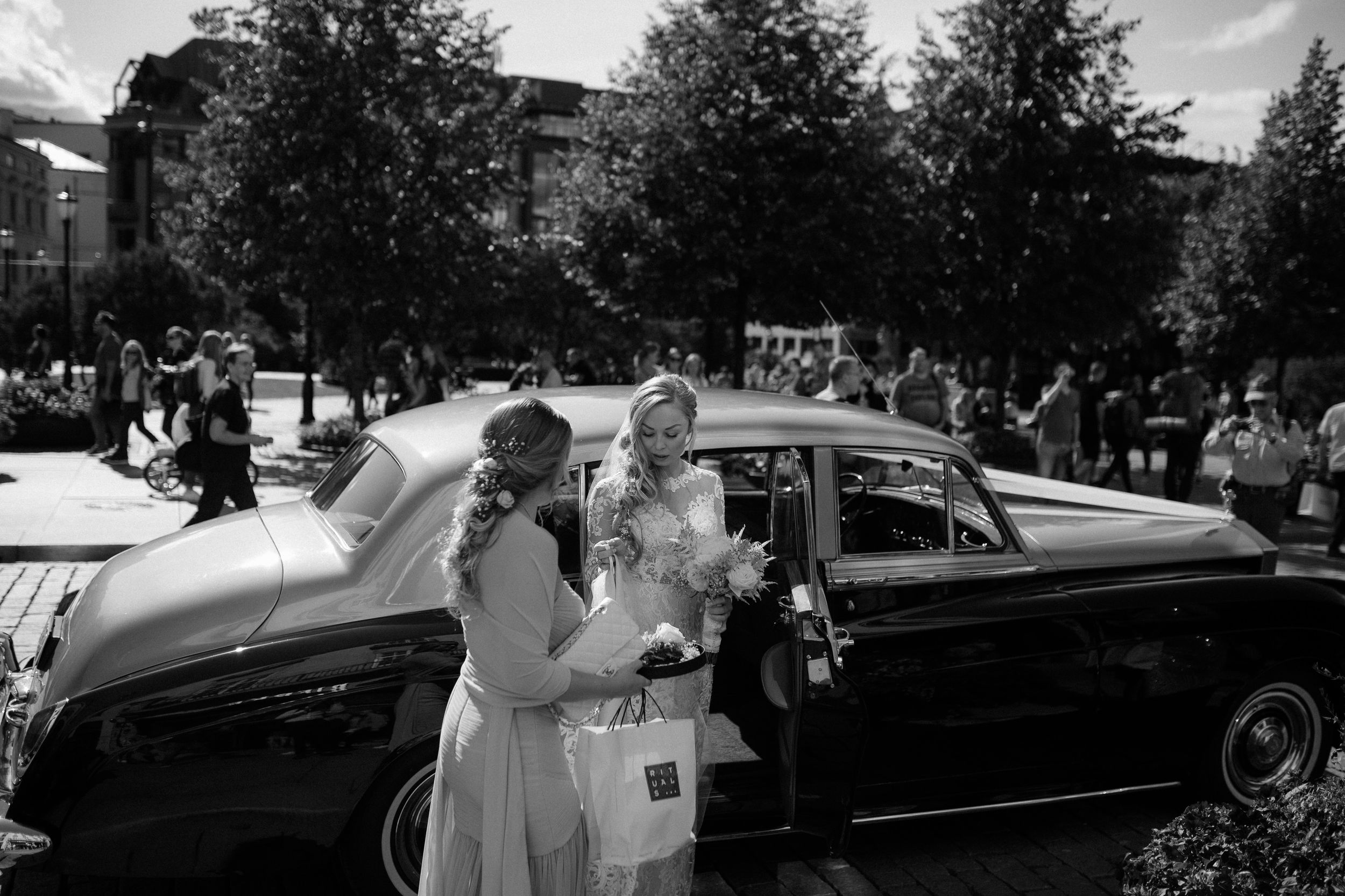 A classic vintage car scene at a wedding celebration captured in elegant black and white photography.