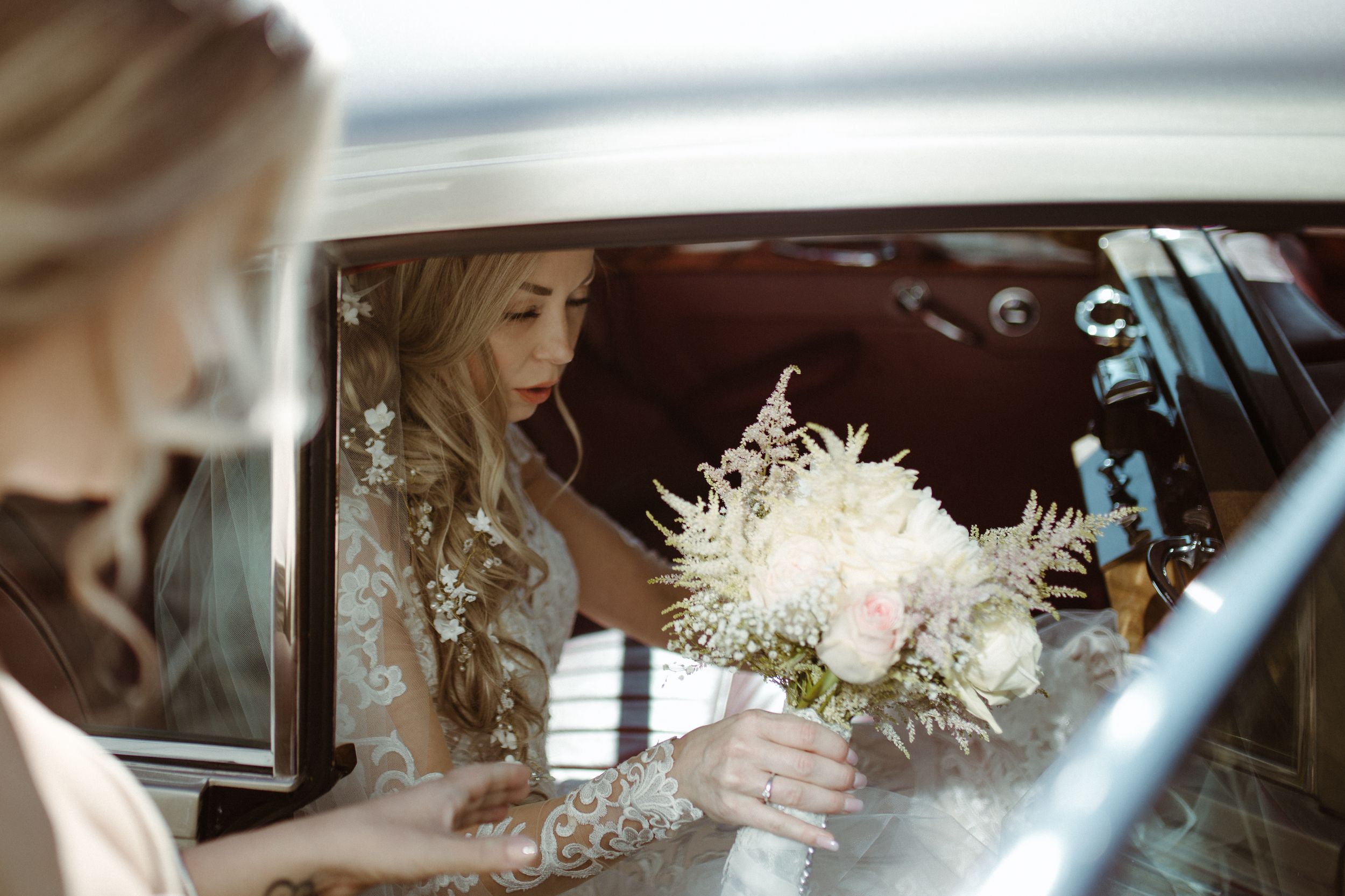 White floral bouquets being held in a car during a wedding day.
