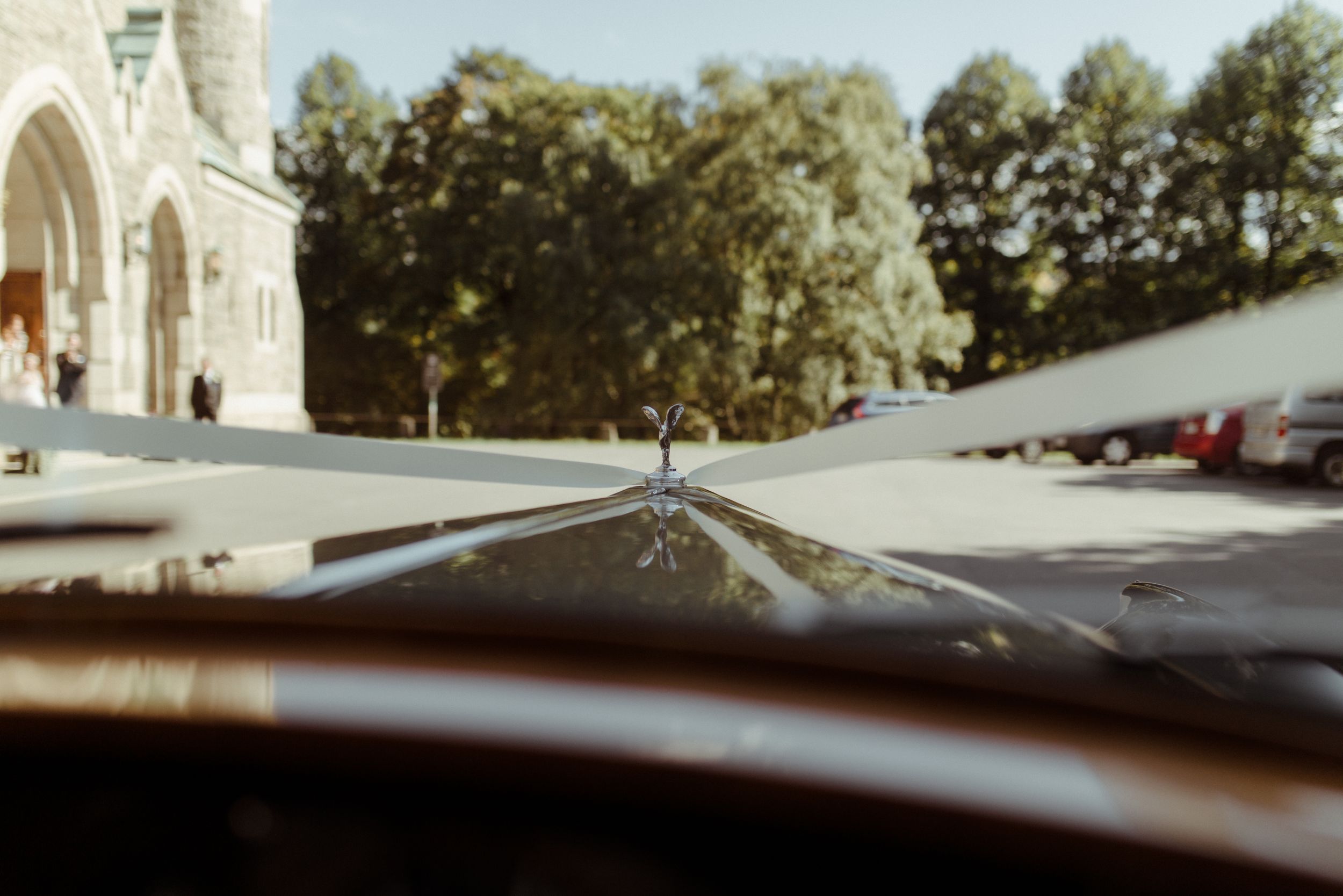 View through a car windshield looking towards a gothic church facade with trees in the background.