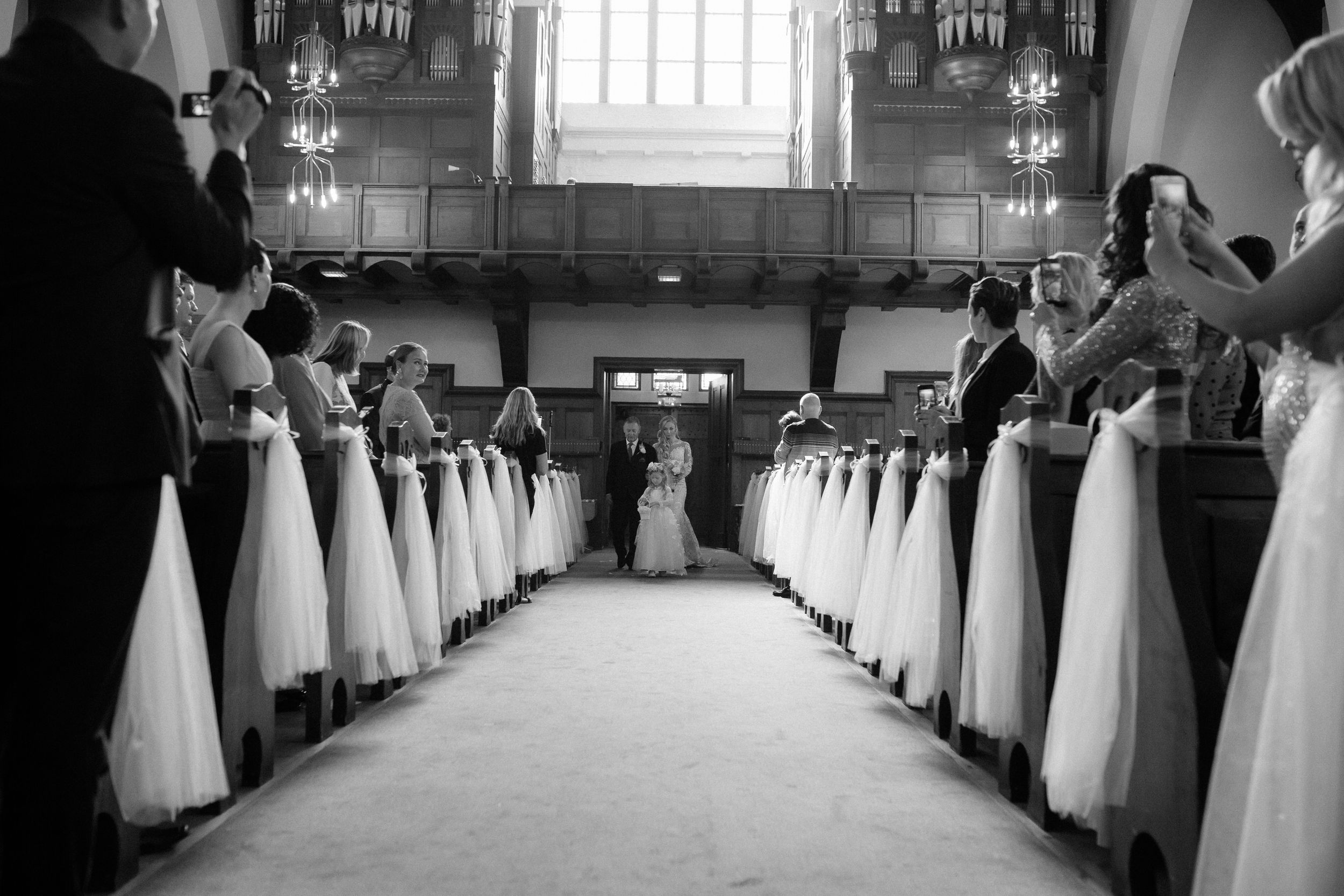 Church aisle decorated with white fabric on pews creating a romantic wedding ceremony setting.