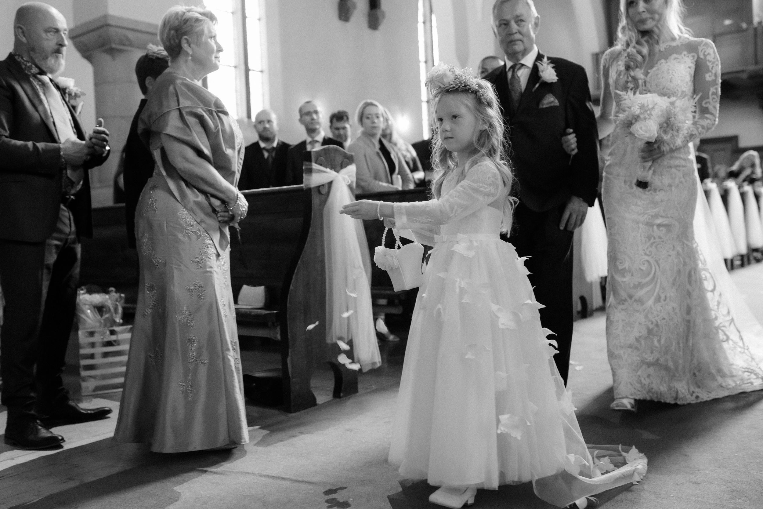 A black and white photo of a young attendant in a white dress during a wedding ceremony in a church.