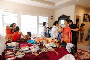 People gather around clothing and items displayed on a red blanket during what appears to be a clothing swap event indoors.