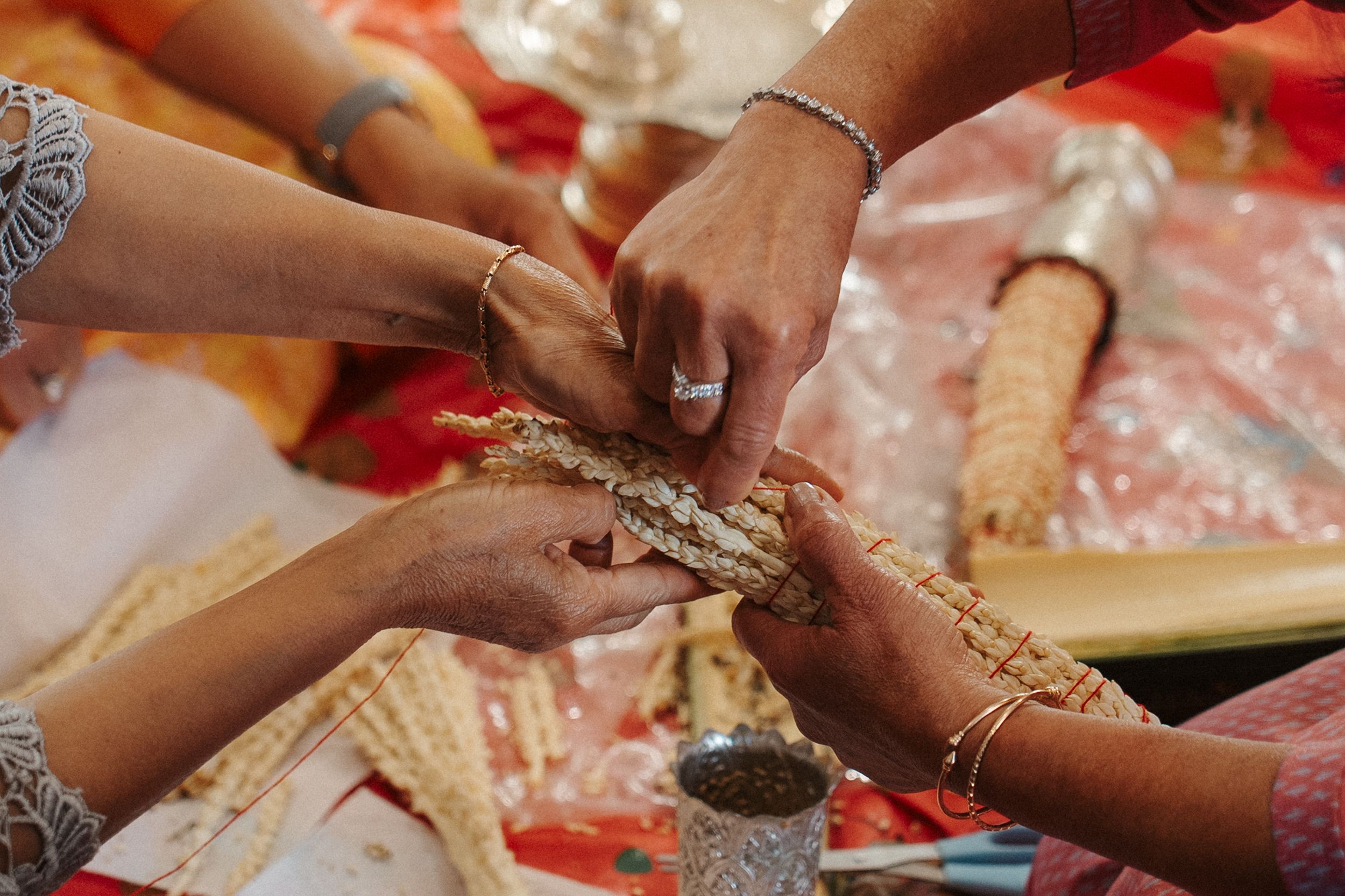 Hands exchanging ceremonial items during a traditional Indian wedding ritual over red and orange decorative cloth.