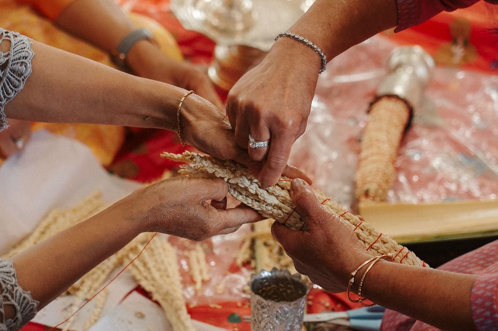 Hands exchanging ceremonial items during a traditional Indian wedding ritual over red and orange decorative cloth.