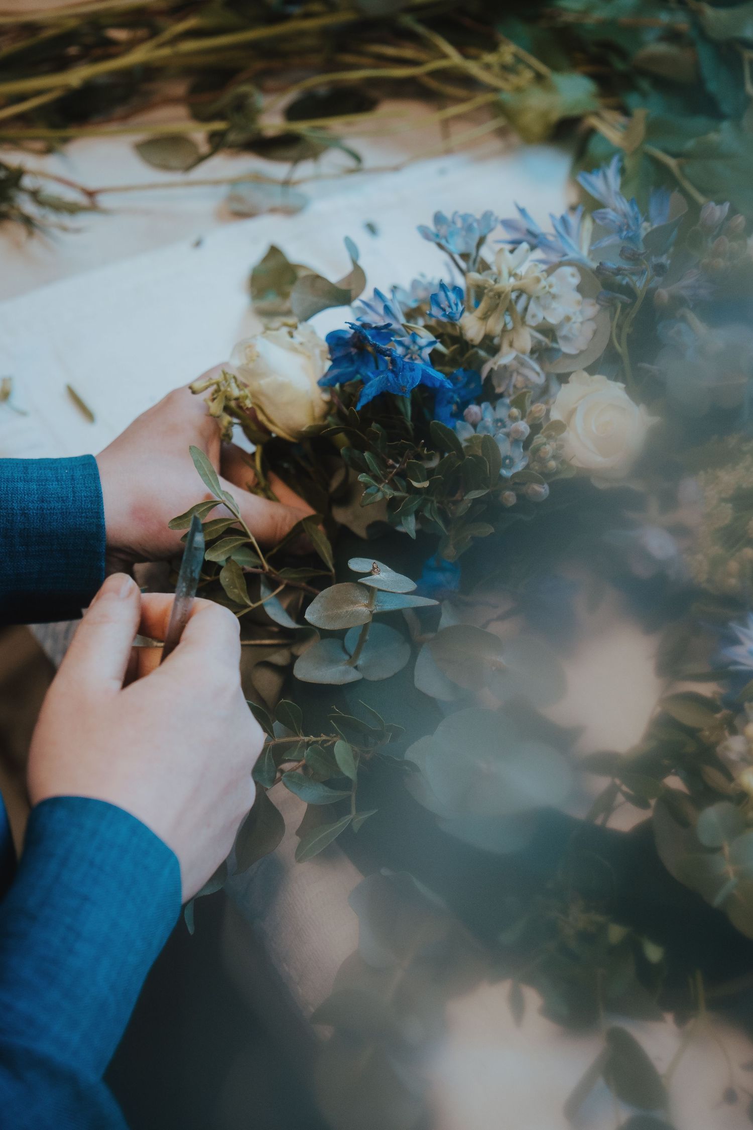Close-up shots of hands arranging dried flowers and leaves on a reflective surface.