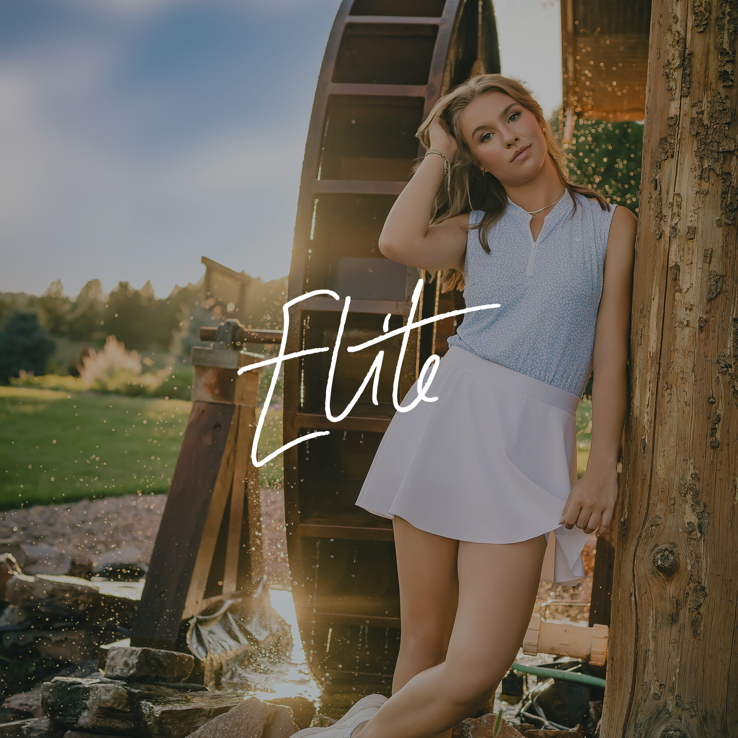 A person poses outdoors in a light blue outfit near a rustic ladder structure on a sunny day.