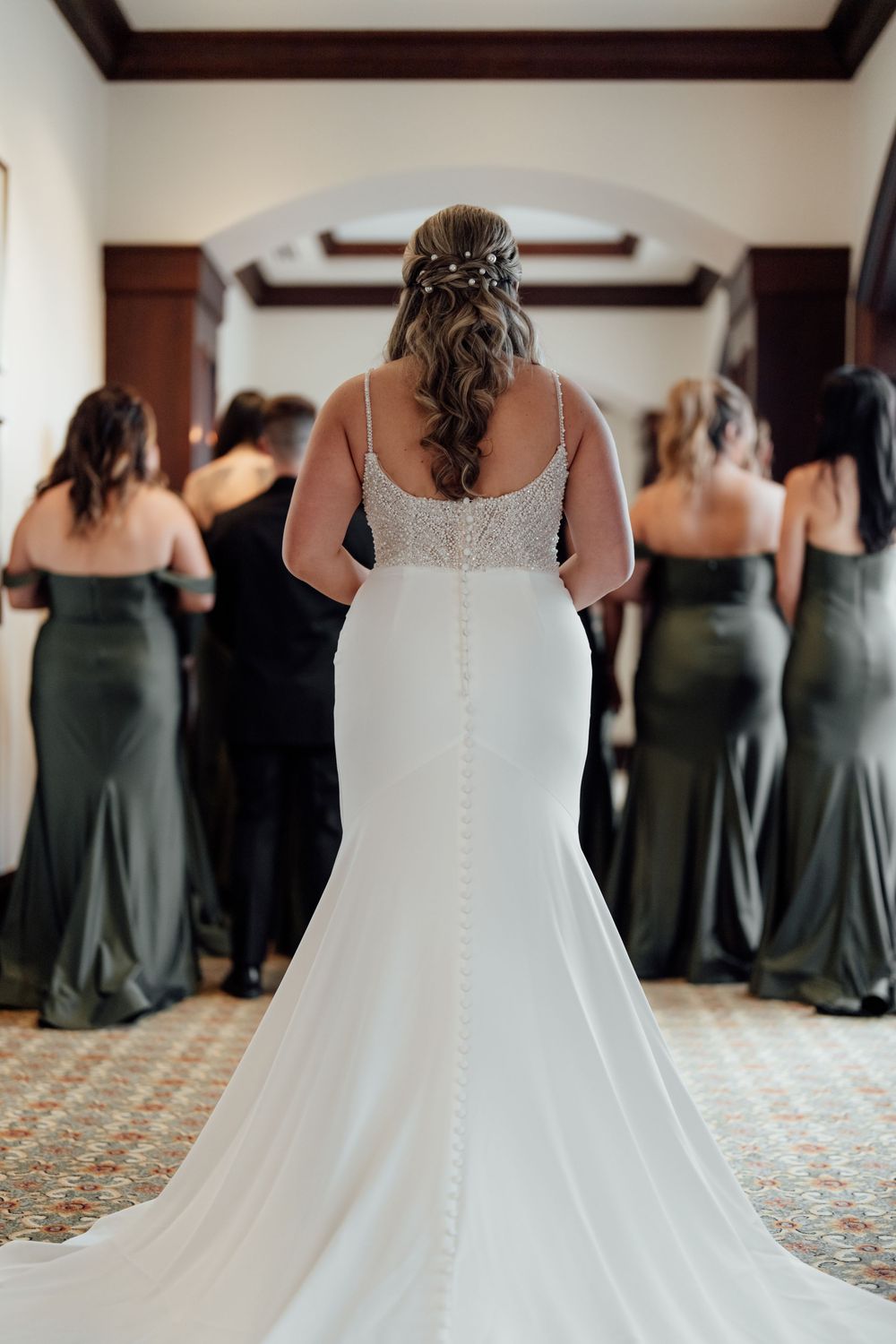 Bridesmaids in sage green dresses line up before a wedding ceremony.