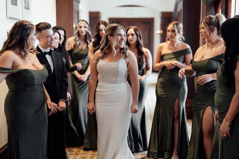 Wedding party members in dark green dresses and white gowns gather together during a celebration.