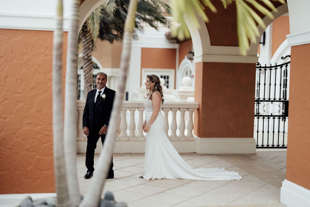 Bride and groom pose together against terracotta walls and white columns at their elegant outdoor wedding venue.