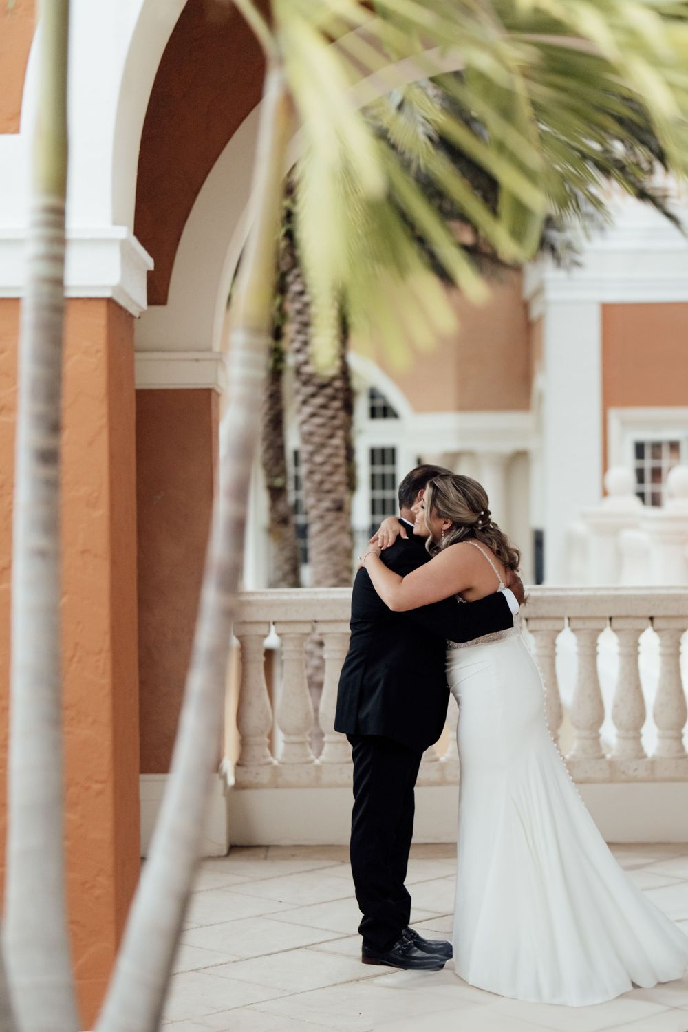First look wedding moment captured under elegant columns with palm trees.