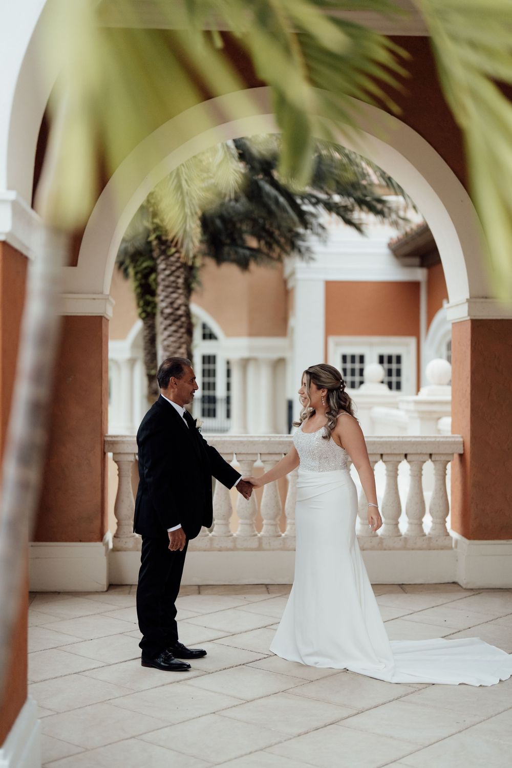 First look between couple at tropical wedding venue with palm trees and arched walkway.