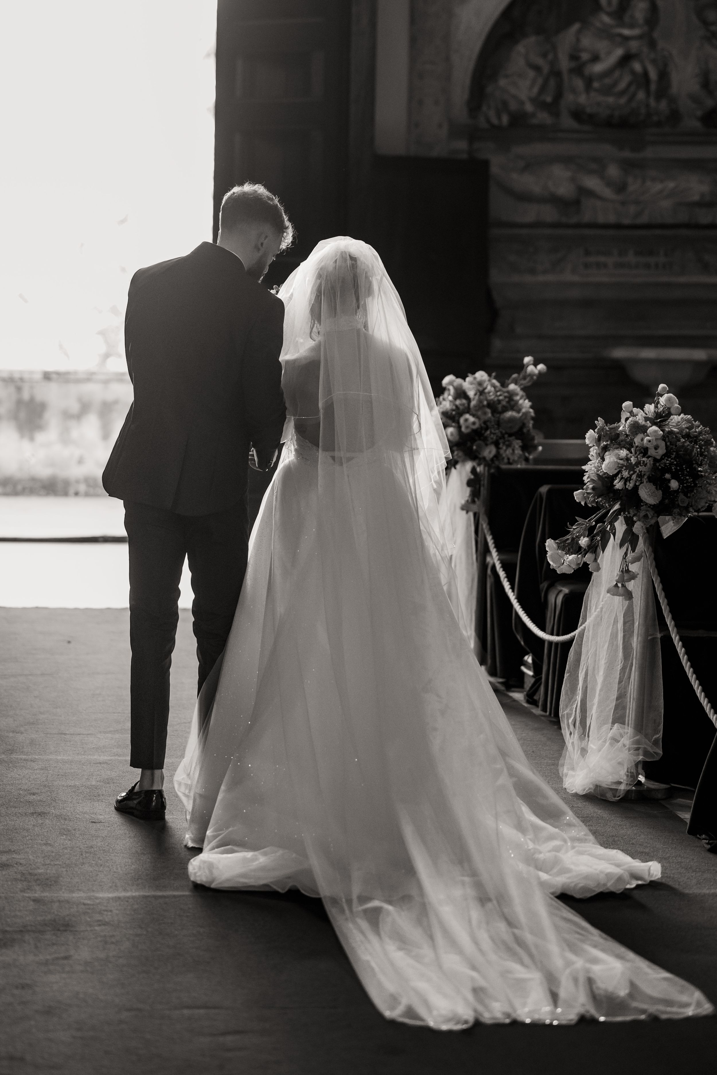 A row of five black and white photos showing a bride and groom walking away together at a wedding ceremony.