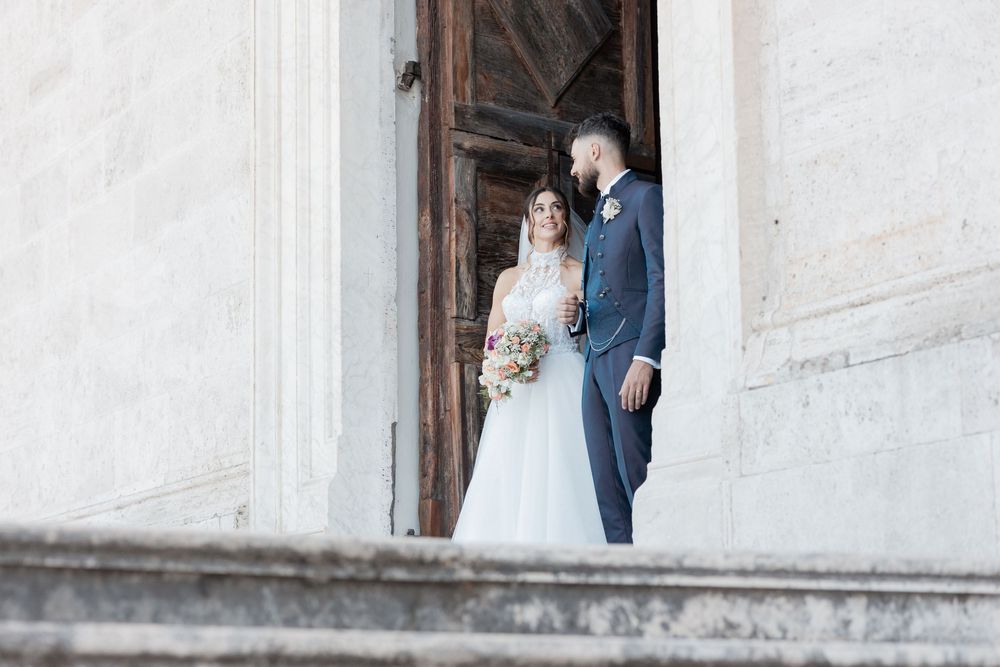 A wedding couple stands framed in the white archway of a historic building entrance.