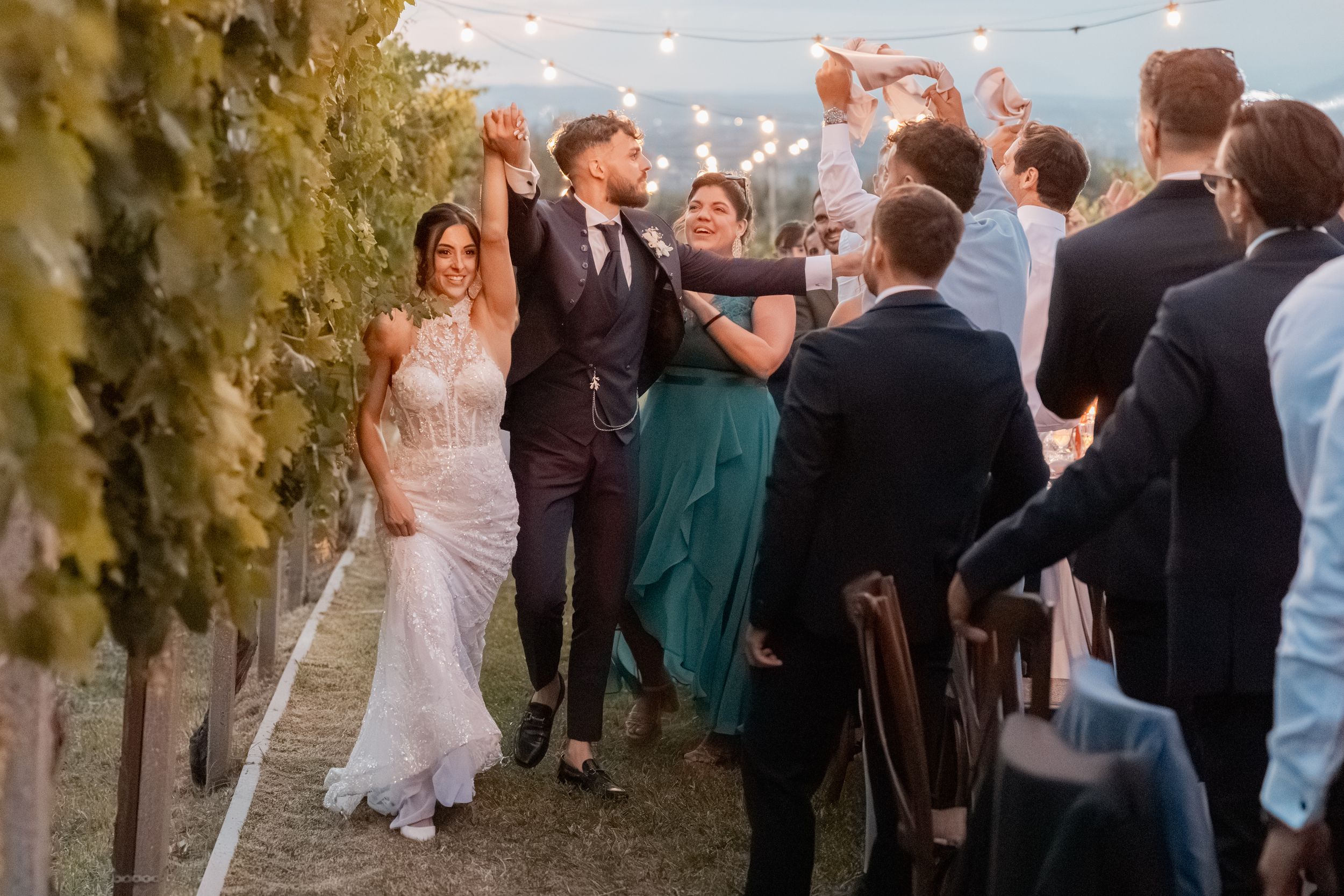 Wedding guests gather outdoors at sunset to celebrate with the newlyweds during their reception.