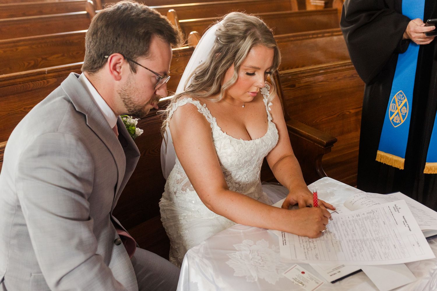 Bride and groom sign marriage documents together at a wooden table during their wedding ceremony.