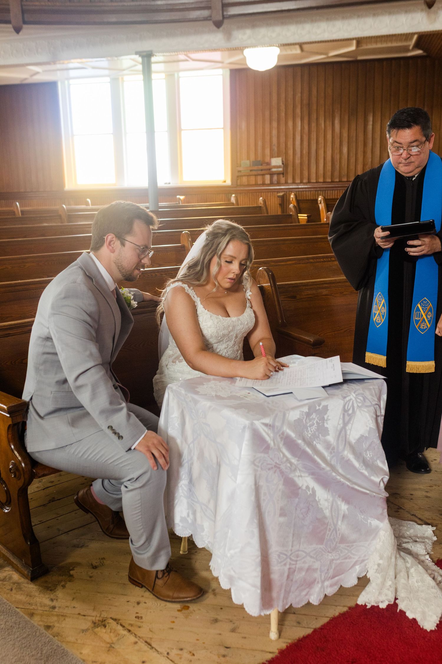 A couple signs marriage documents during their rustic barn wedding ceremony with an officiant in blue robes present.