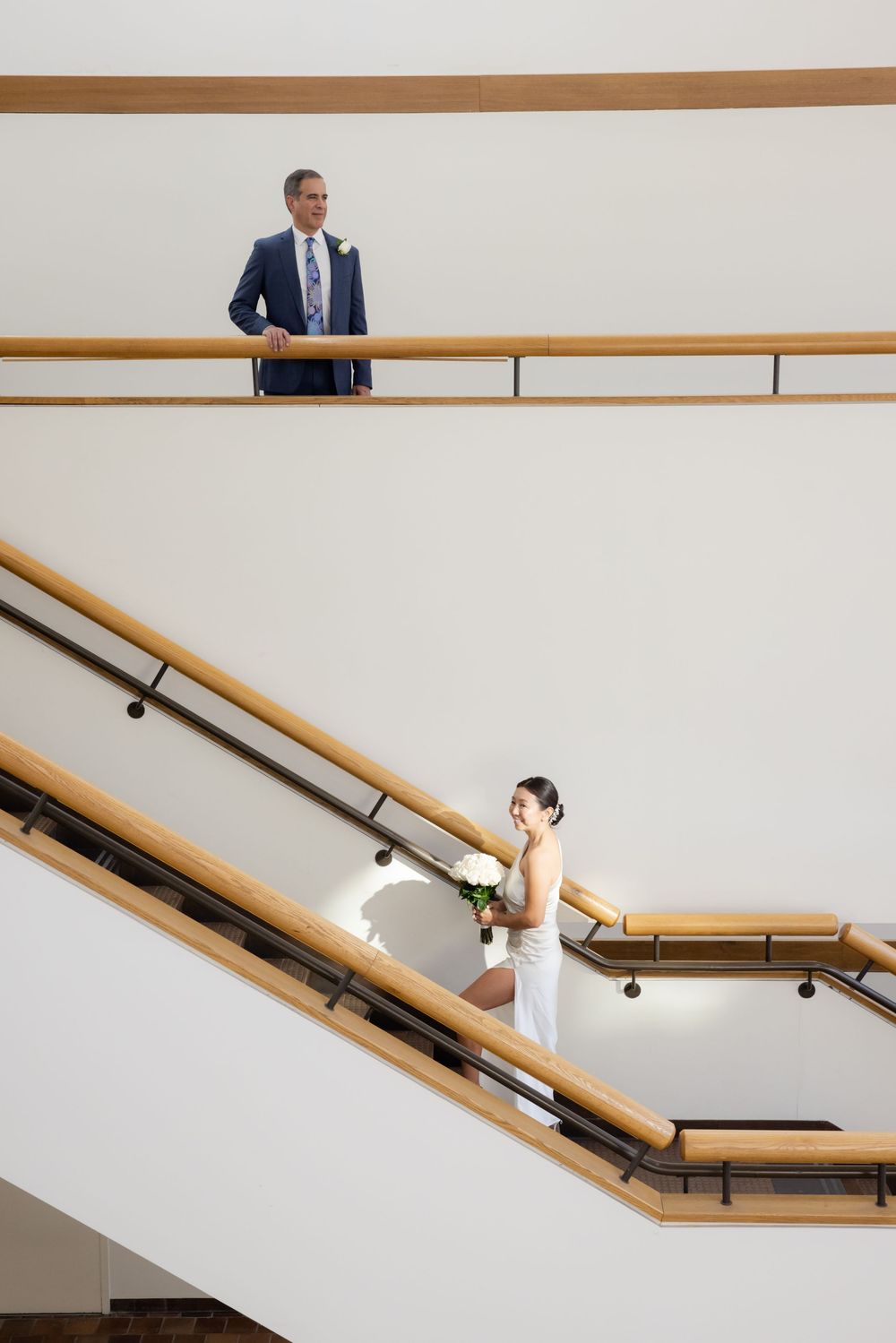 Minimalist white interior stairwell with wooden handrail forming a geometric pattern against clean walls.