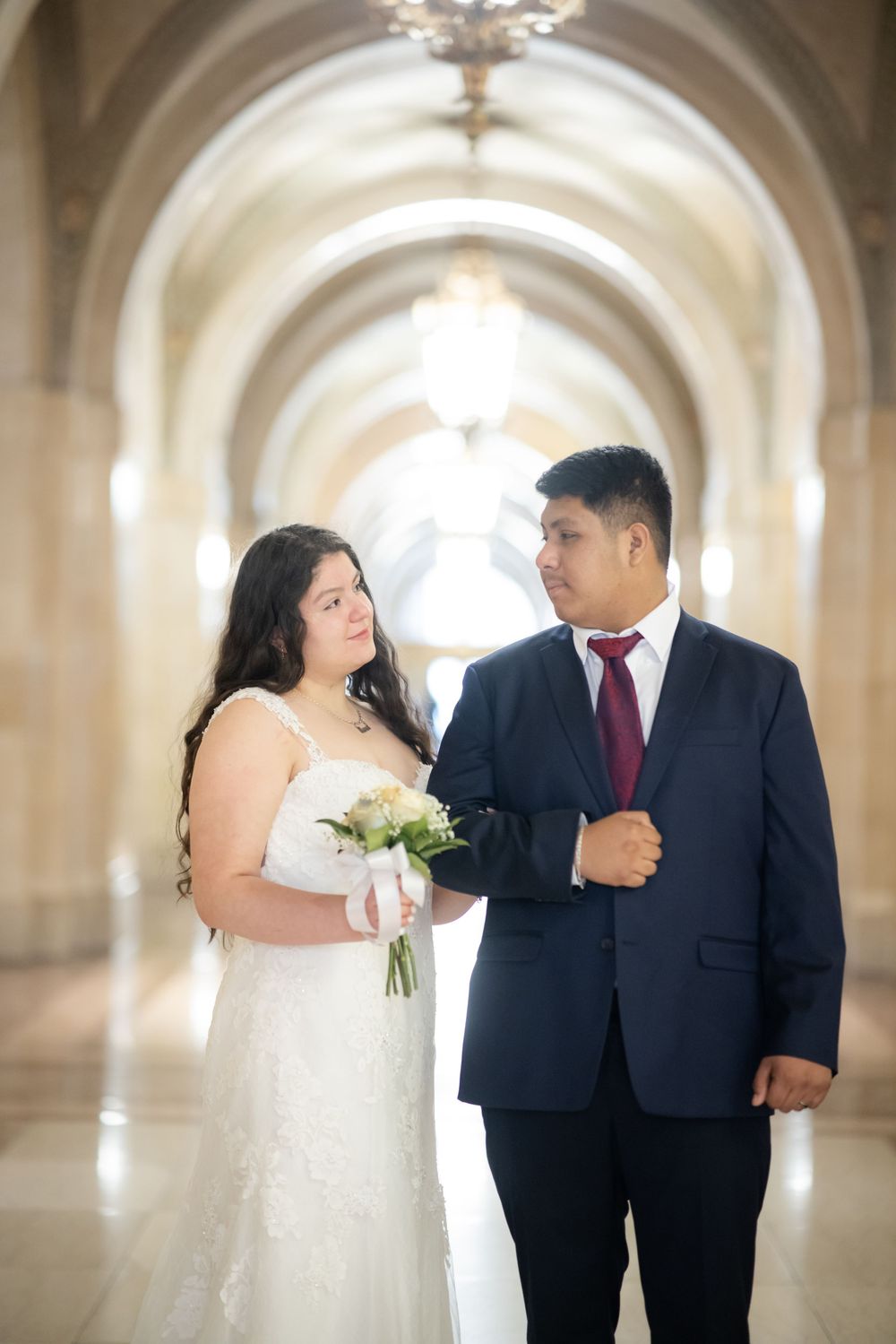 A couple in wedding attire share intimate moments while walking through an elegant arched hallway.