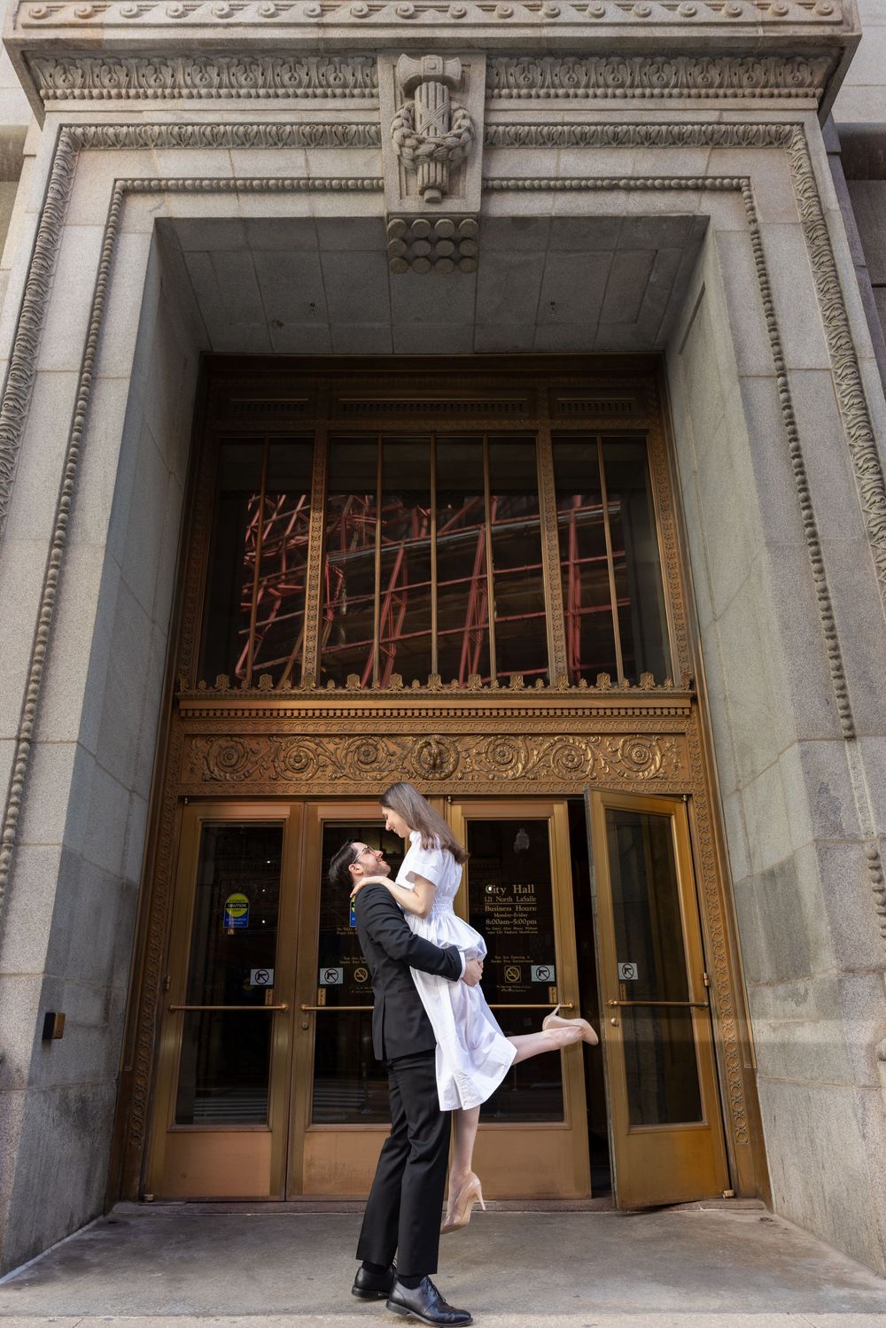 Couples embrace in a dip pose against an ornate classic stone building entrance with decorative architectural details.