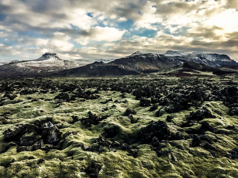 Aerial panoramic view of rugged green moss-covered volcanic landscape in Iceland under dramatic cloudy skies.