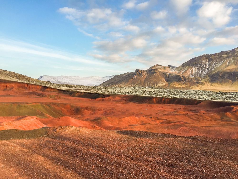 Panoramic mountain landscape with dramatic clouds set against rugged desert peaks and red sandstone formations.