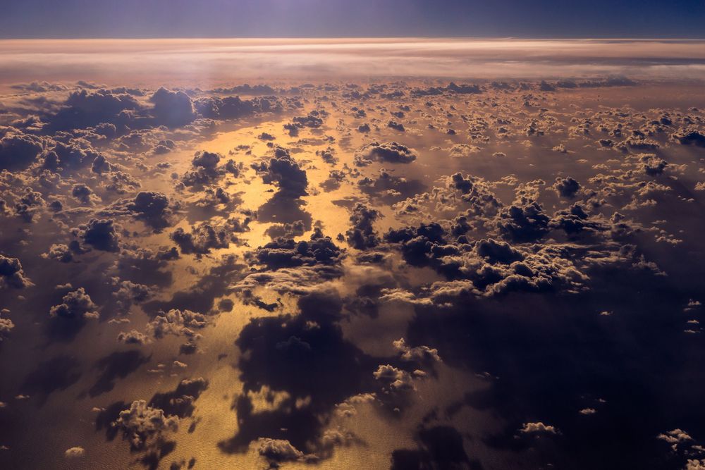 Dramatic aerial view of clouds at sunset with golden sunlight filtering through the dense cloud formations.