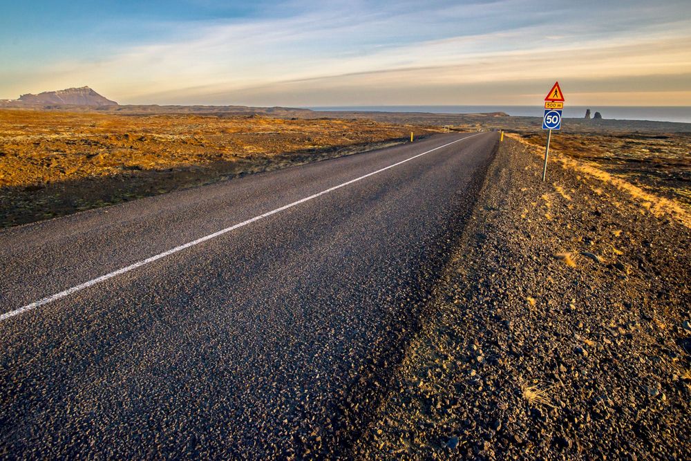 Scenic panorama of empty desert highway stretches toward distant mountains at sunset with golden light.