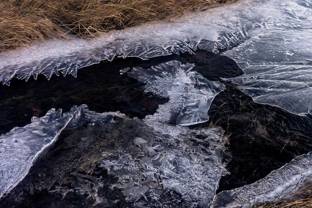 Aerial view of a melting glacier showing ice formations and rugged terrain patterns in a mountainous landscape.